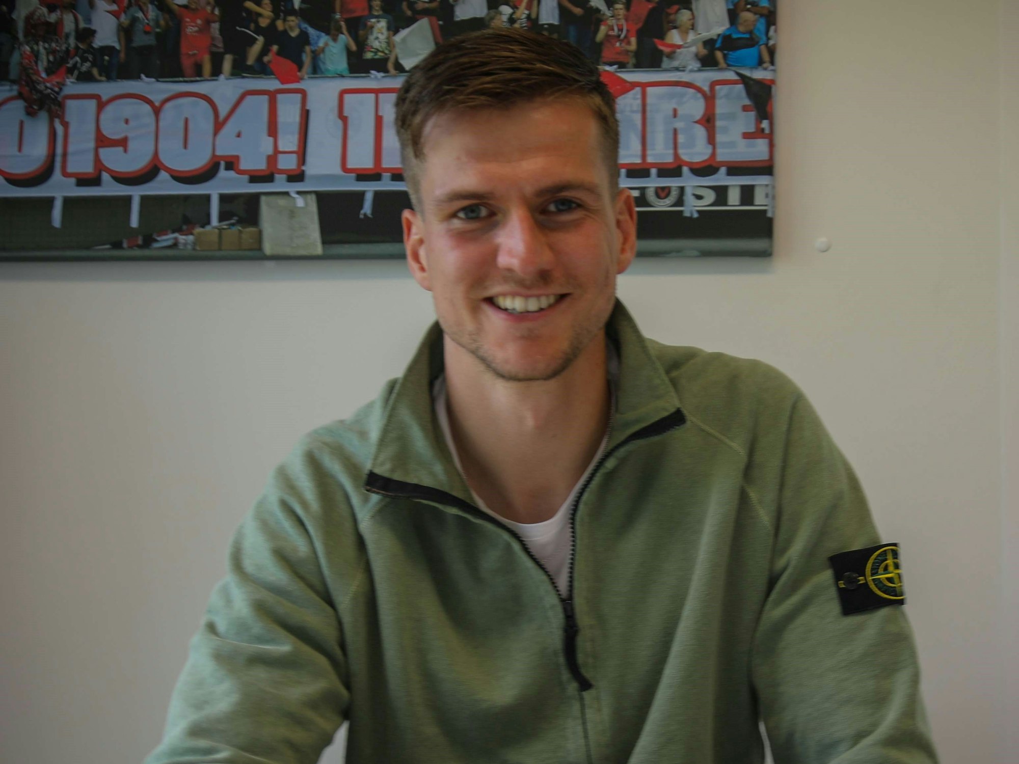 Moritz Fritz lächelt bei der Vertragsunterschrift bei Viktoria Köln in die Kamera.