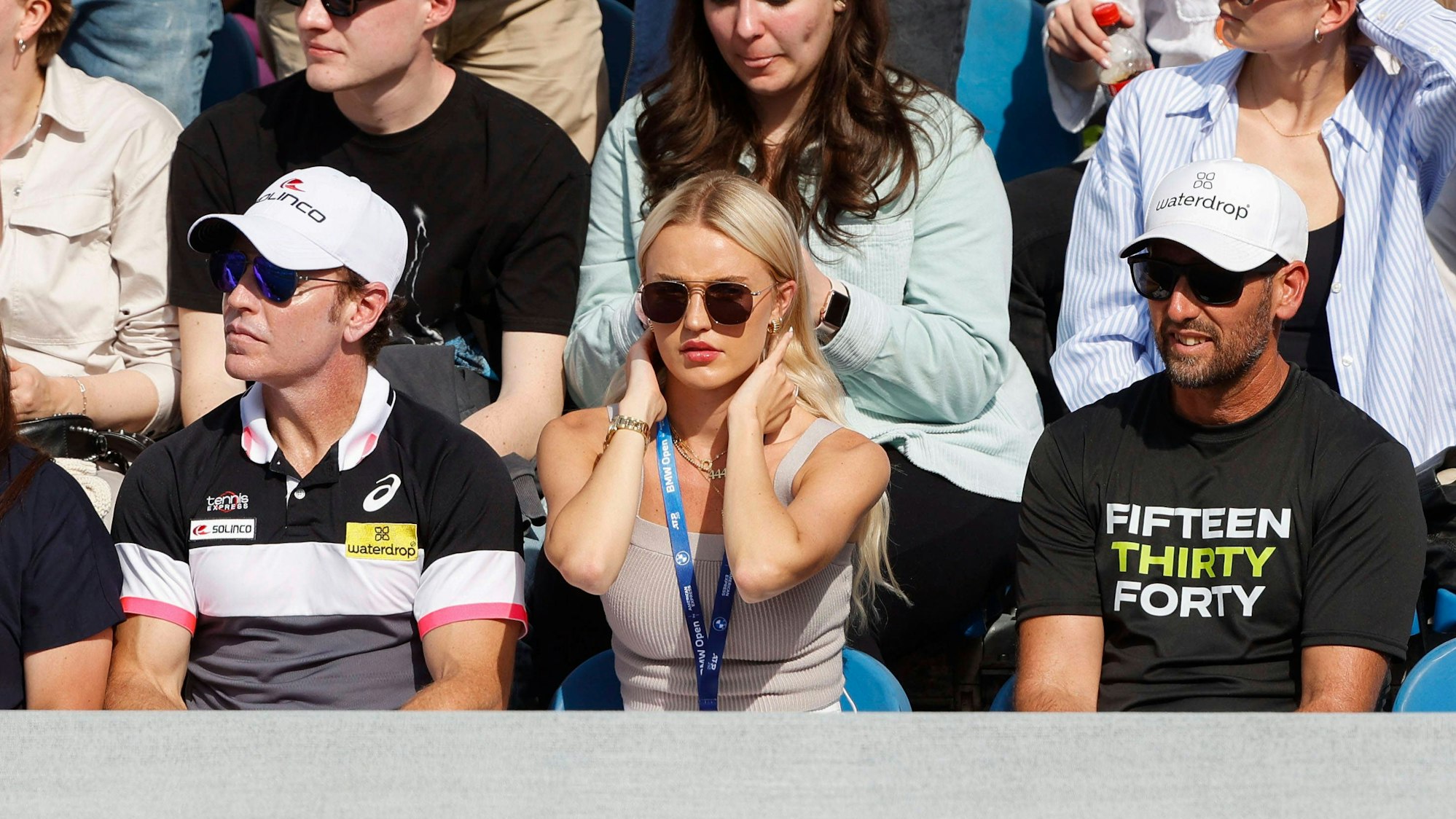 Morgan Riddle (M.) sitzt mit Sonnenbrille auf der Tribüne bei der Partie zwischen Taylor Fritz und Botic van de Zandschulp.