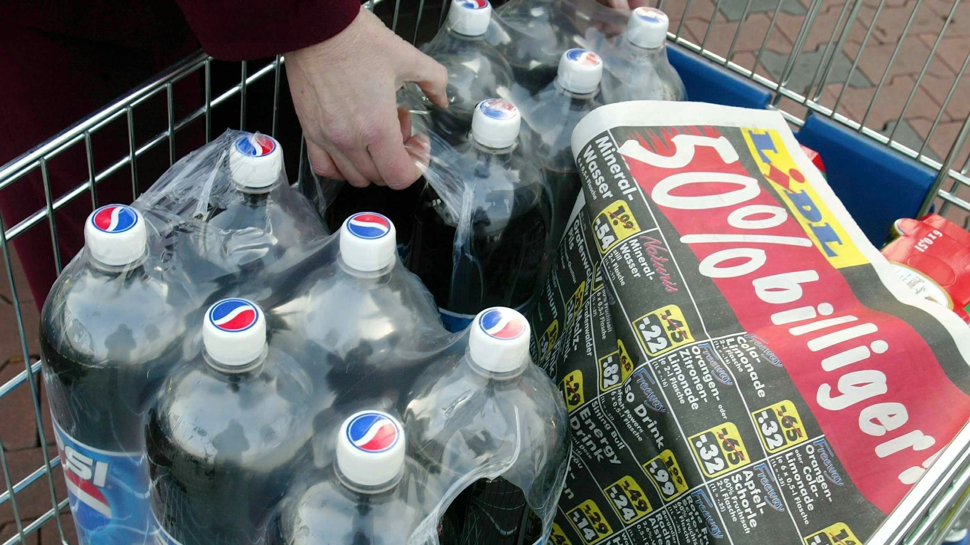 Eine Frau nimmt vor einem Lidl-Supermarkt Einwegflaschen und Dosen aus ihrem Einkaufswagen.