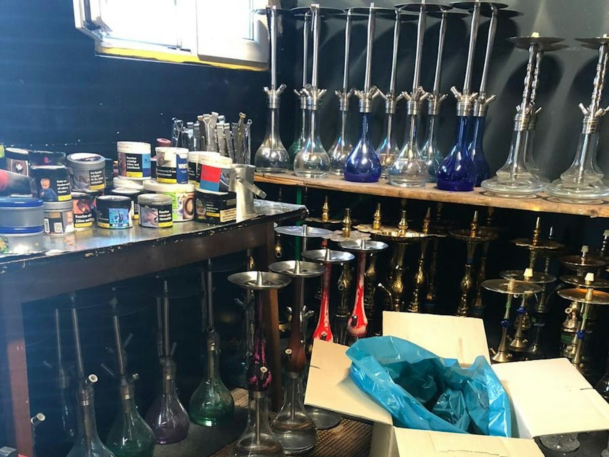 Auf Tischen stehen Shisha-Pfeifen und Tabakdosen.