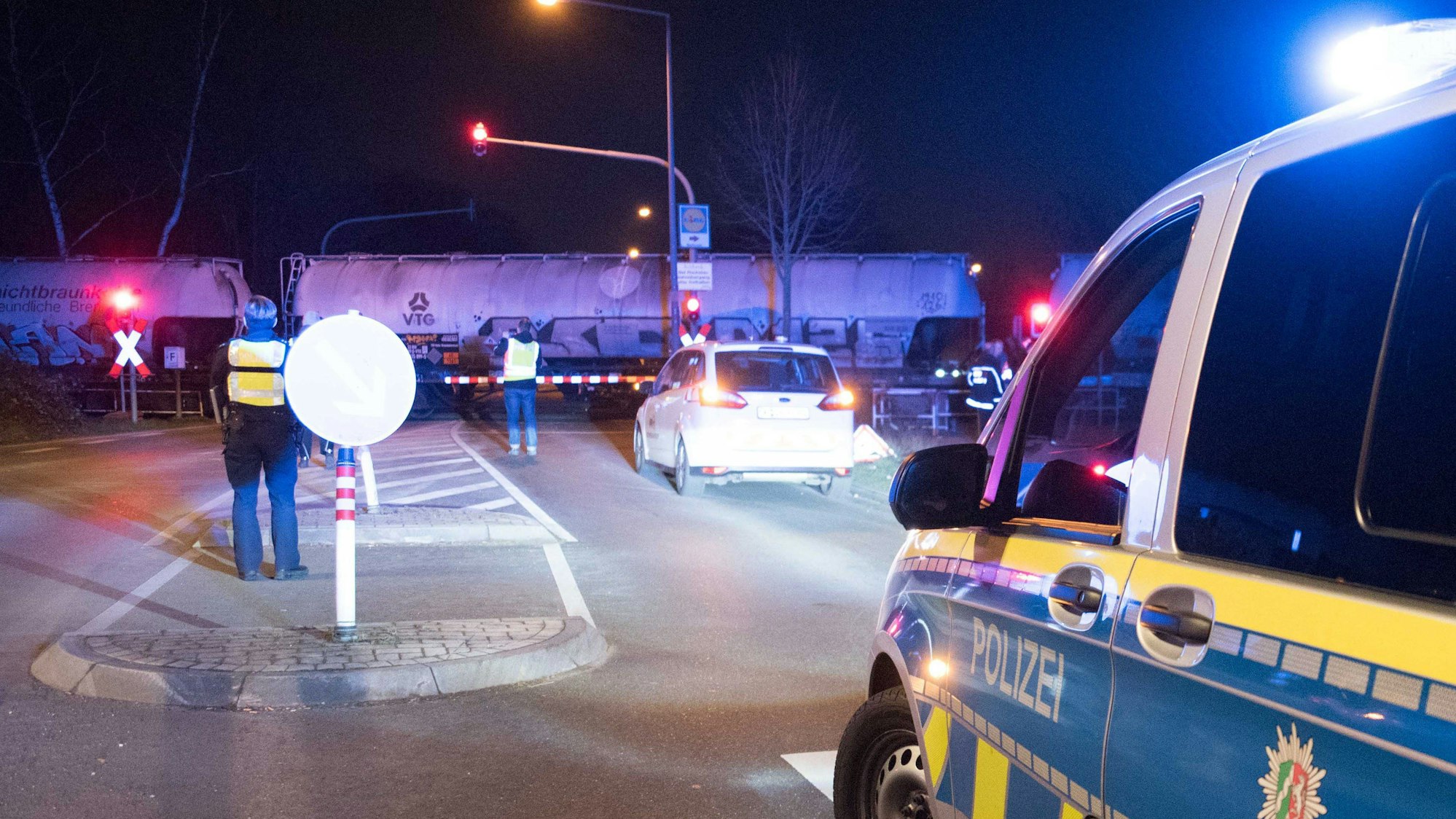Ein Polizei-Auto und mehrere Fußgänger stehen vor einem Bahnübergang.