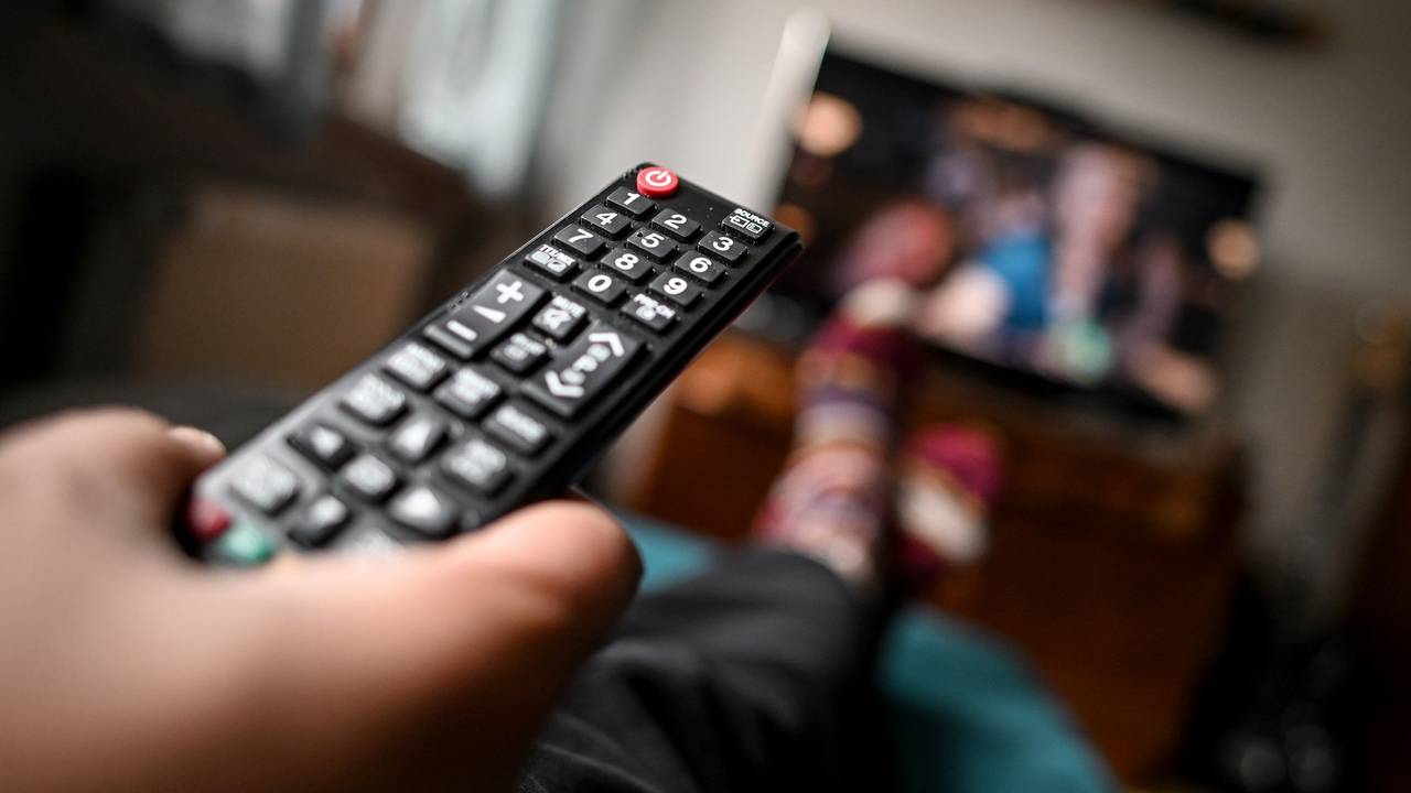Ein junger Mann sitzt mit einer Fernbedienung vor dem Fernseher.