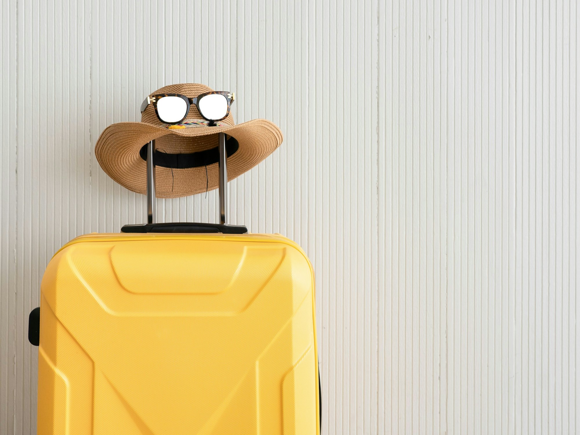 Ein gelber Koffer samt Strohhut und Sonnenbrille stehr abreisebereit parat.