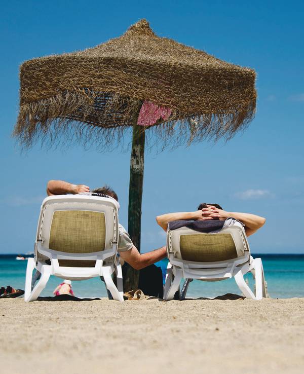 Urlauber liegen auf Sonnenliegen an einem Strand.