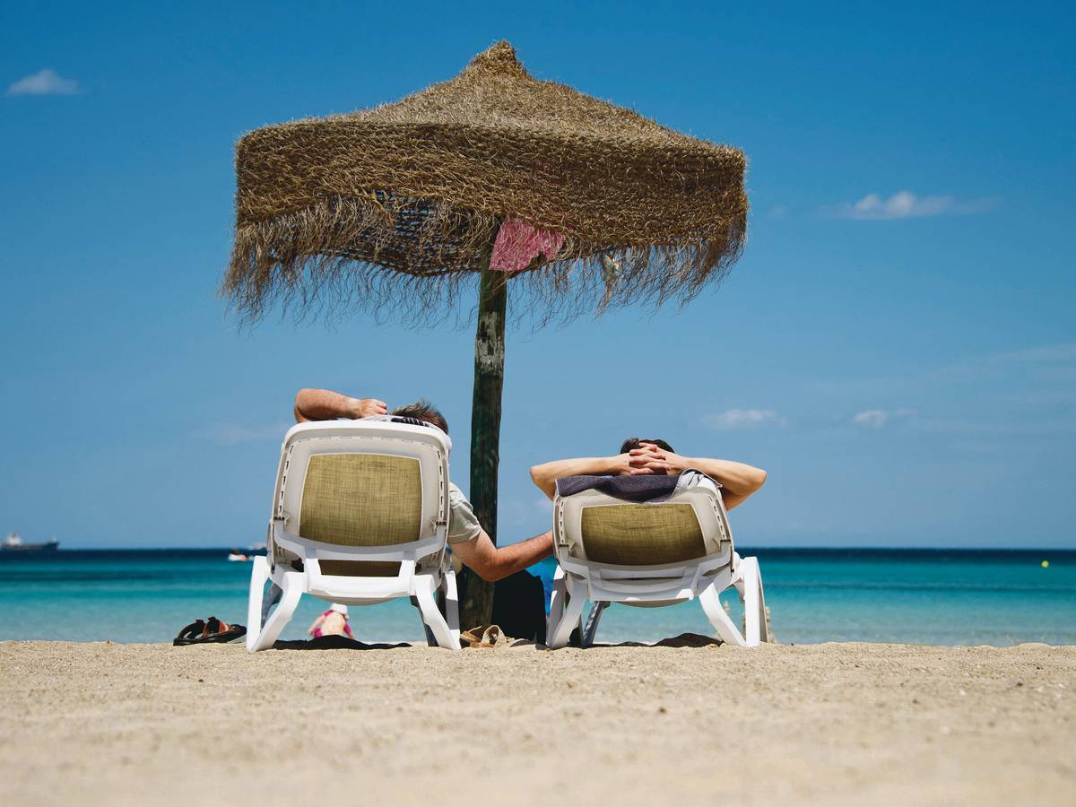 Urlauber liegen auf Sonnenliegen an einem Strand.