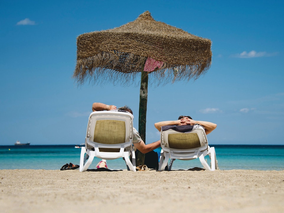 Urlauber liegen auf Sonnenliegen an einem Strand.