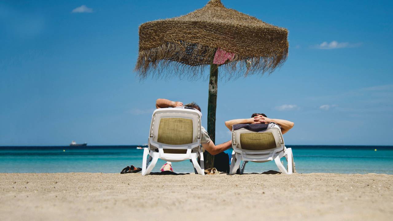 Urlauber liegen auf Sonnenliegen an einem Strand.