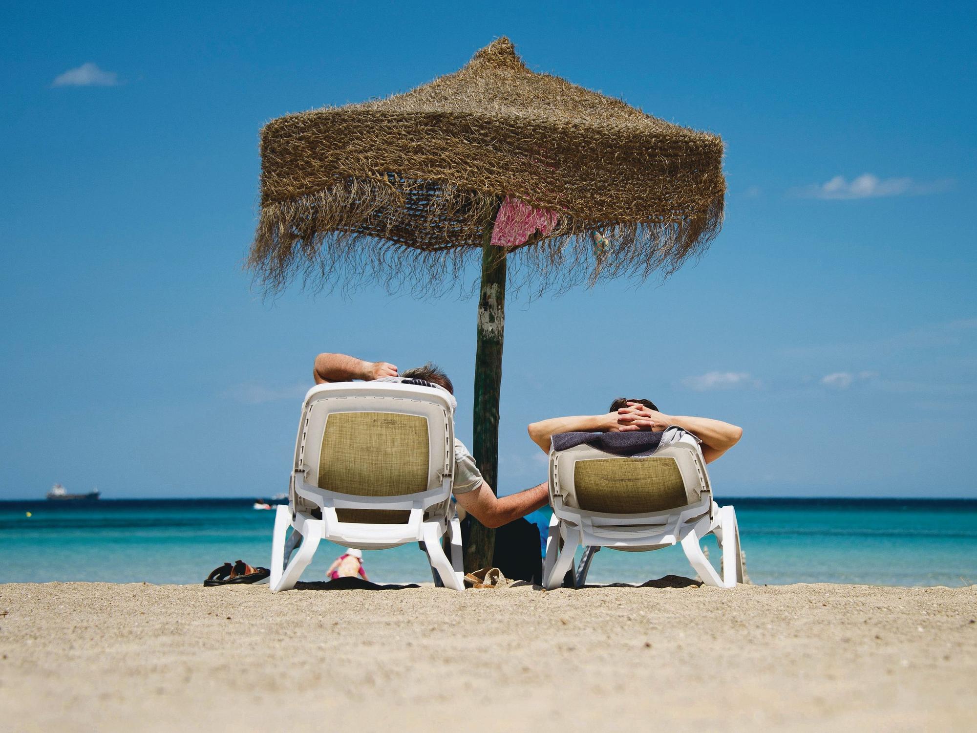 Urlauber liegen auf Sonnenliegen an einem Strand.