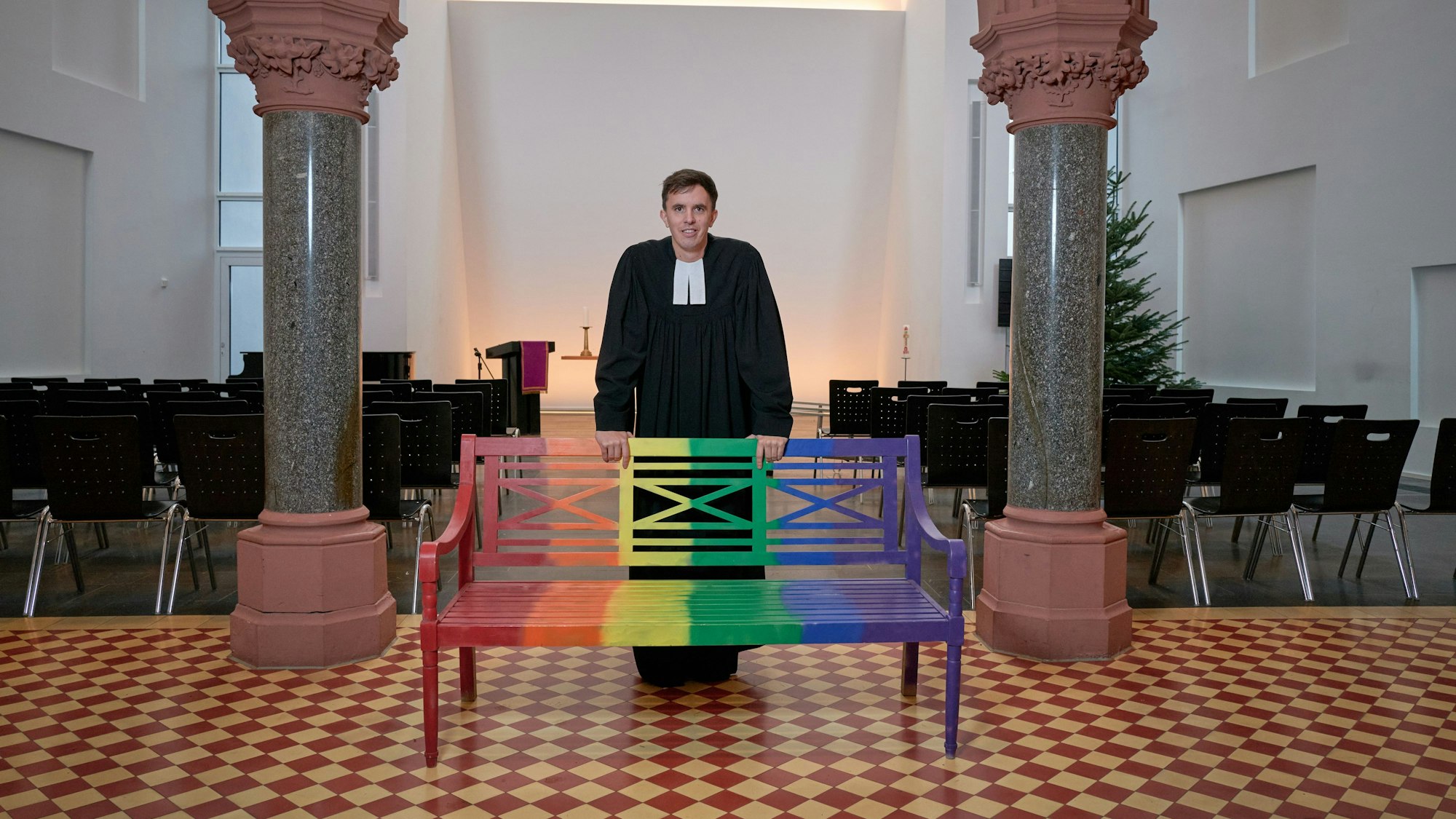 Pastor Tim Lahr steht an einer bunten Bank in der Christuskirche in Köln.