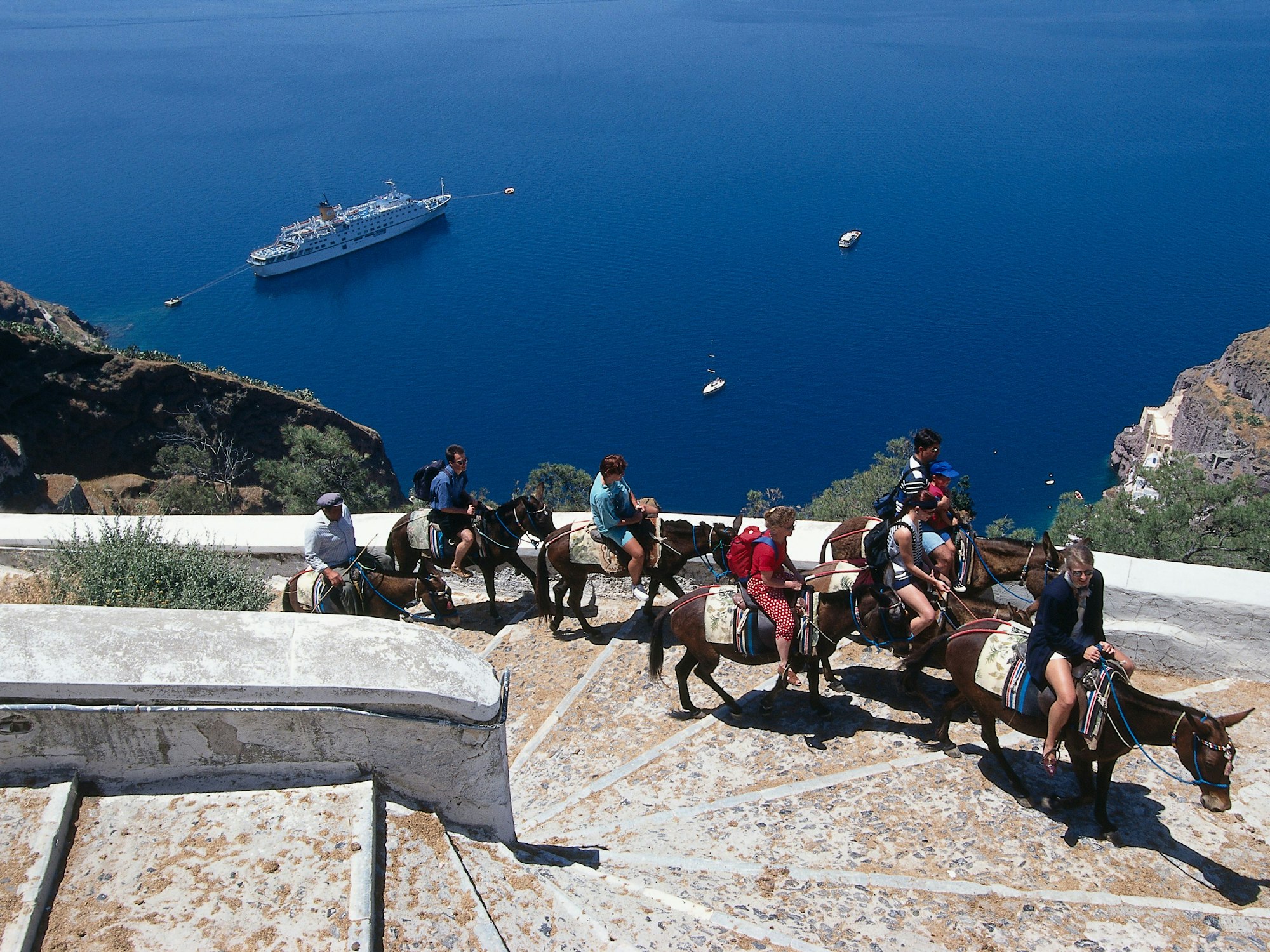 Hier zu sehen, eine Gruppe Touristen auf mehreren Eseln erklimmen einen Berg auf der Insel Santorin in Griechenland.