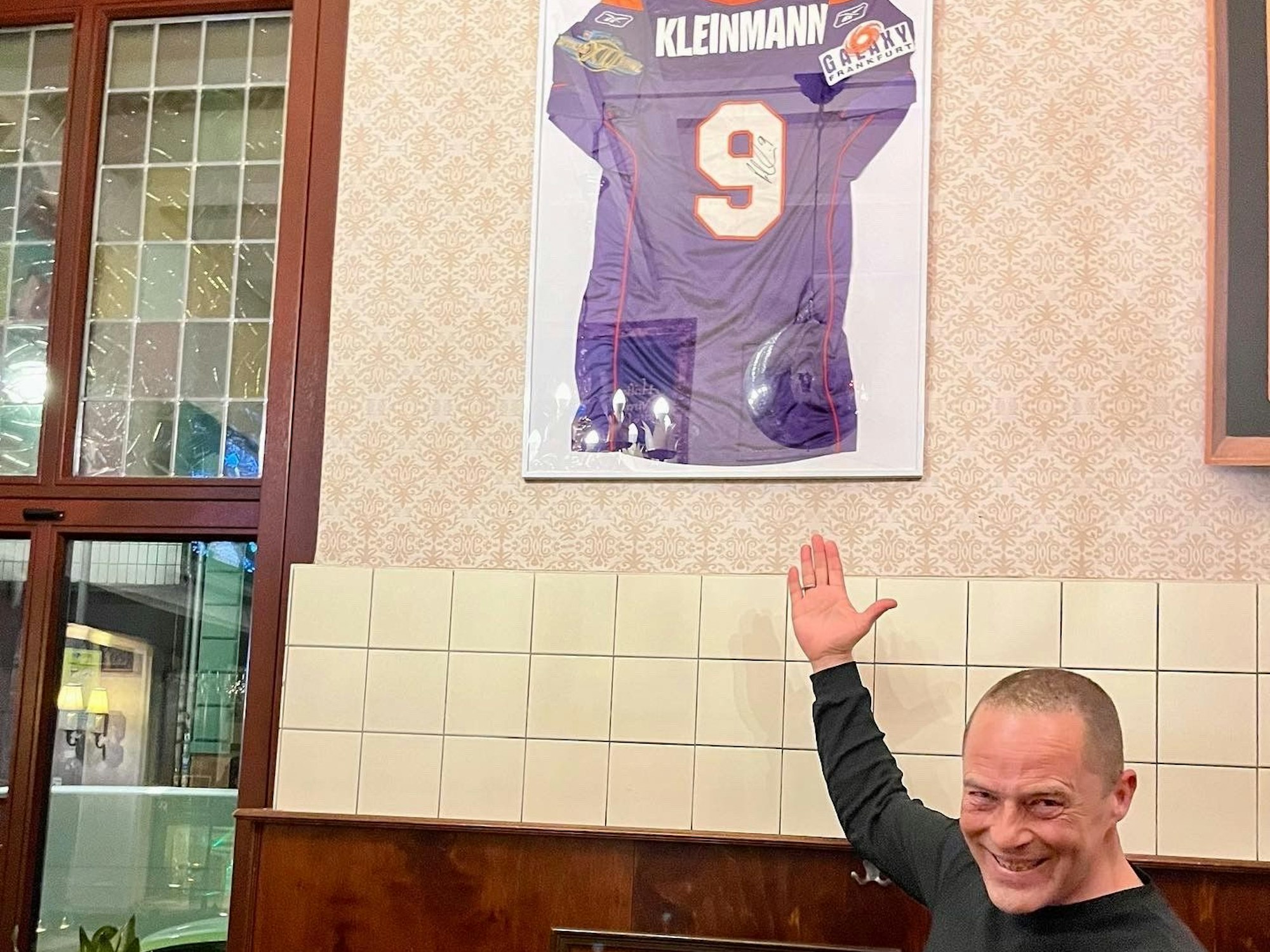 Ex-Footballspieler Ralf Kleinmann zeigt auf sein Trikot, das jetzt in der Gaststätte hängt.