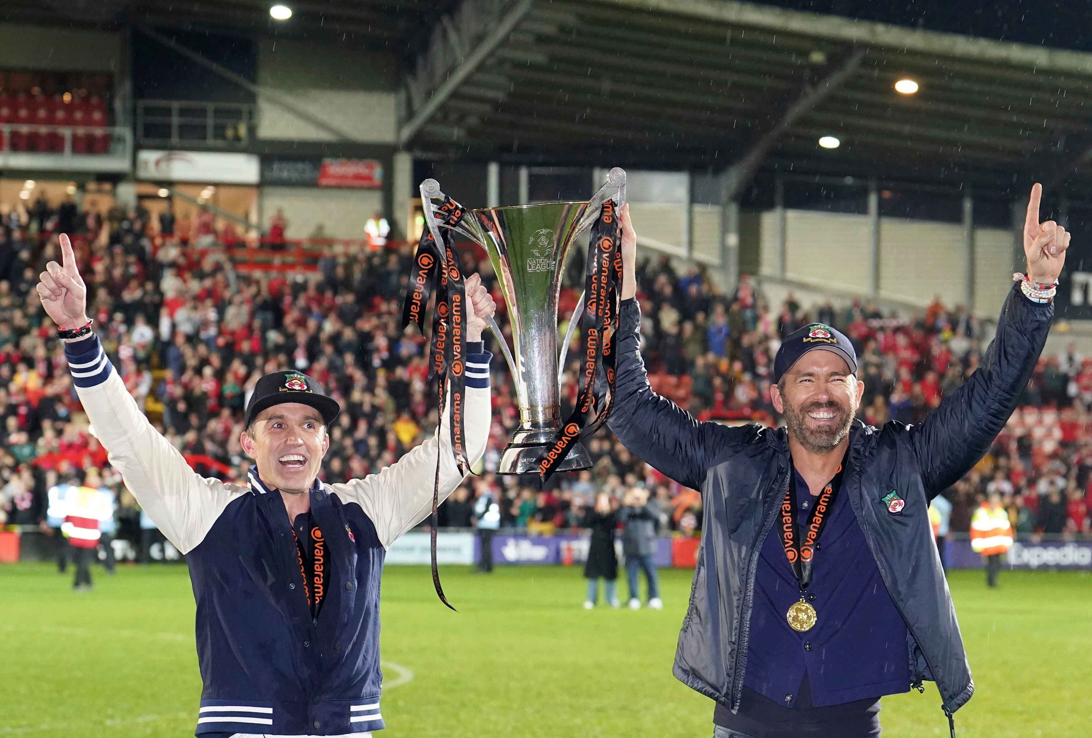 Die Wrexham-Besitzer Rob McElhenney (l.) und Ryan Reynolds stemmen die Meister-Trophäe in die Luft