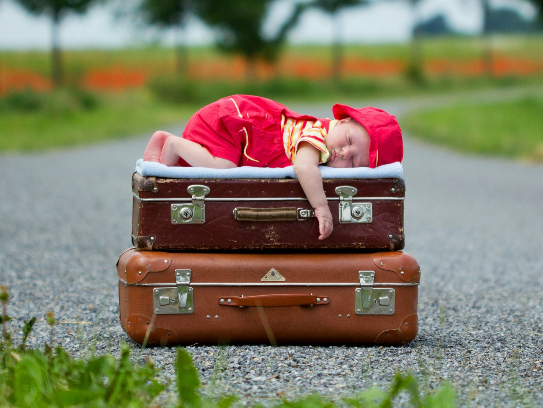 Packliste für den Urlaub: Dieses Baby schläft selig auf gepackten Koffern.