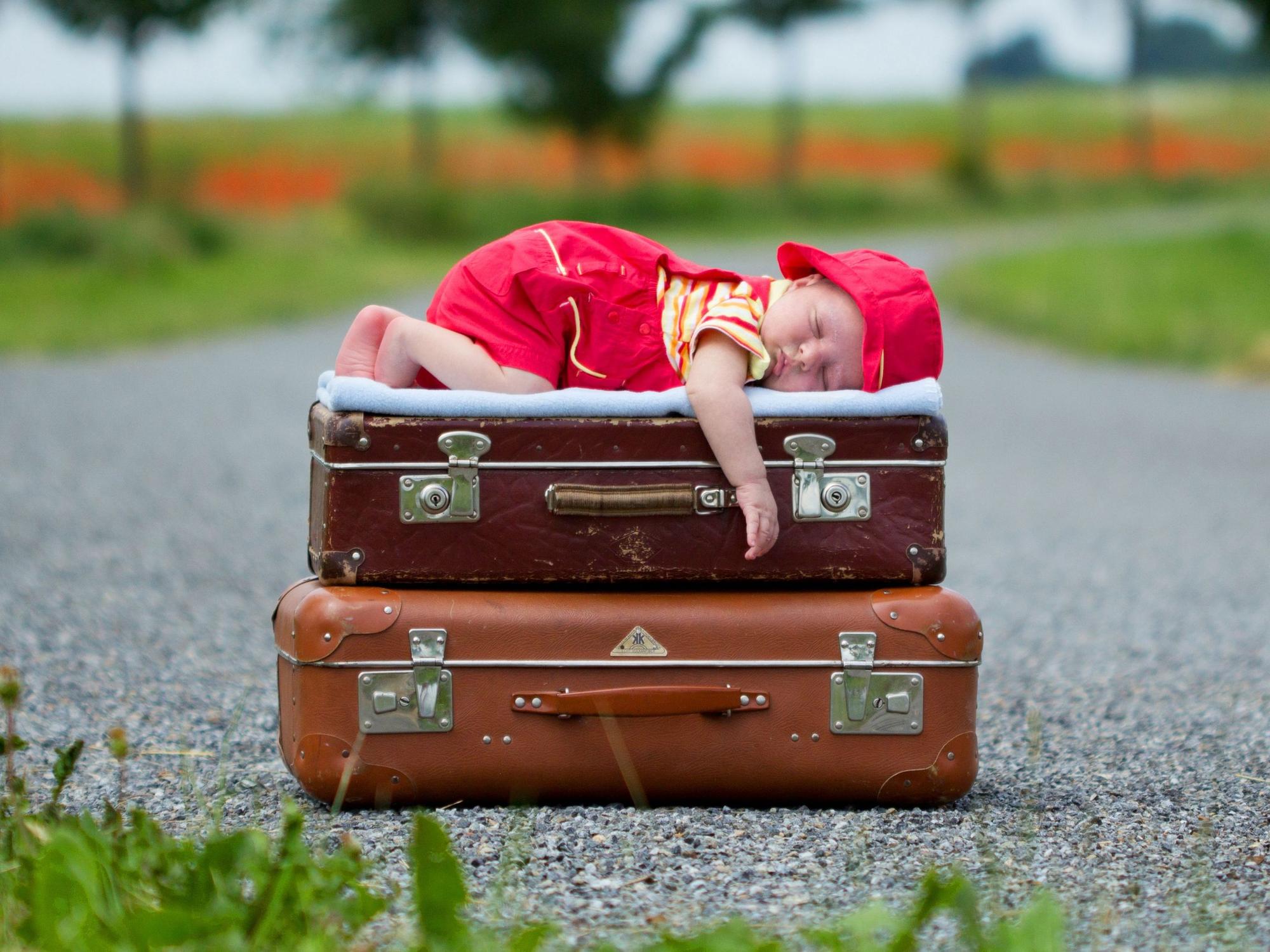 Packliste für den Urlaub: Dieses Baby schläft selig auf gepackten Koffern.
