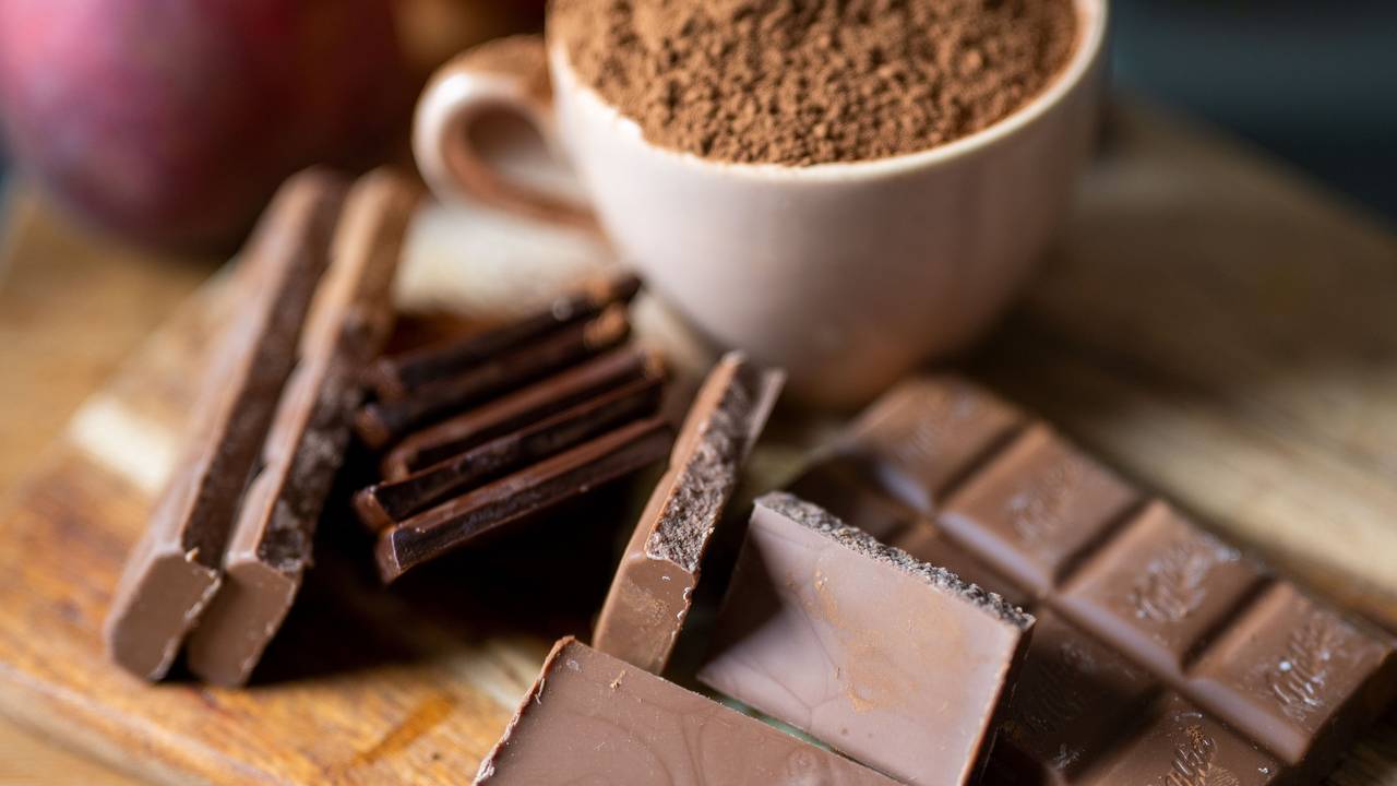 Vollmilchschokolade liegt neben einer mit Kakaopulver gefüllten Tasse auf einem Holzbrett in der Küche, hier im September 2021 in Berlin.