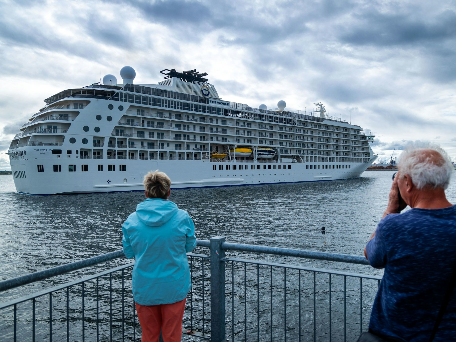 Passanten und Passantinnen beobachten von der Seebrücke aus das Einlaufen des Luxusliners „The World“ in den Seehafen Wismar im Juli 2022.