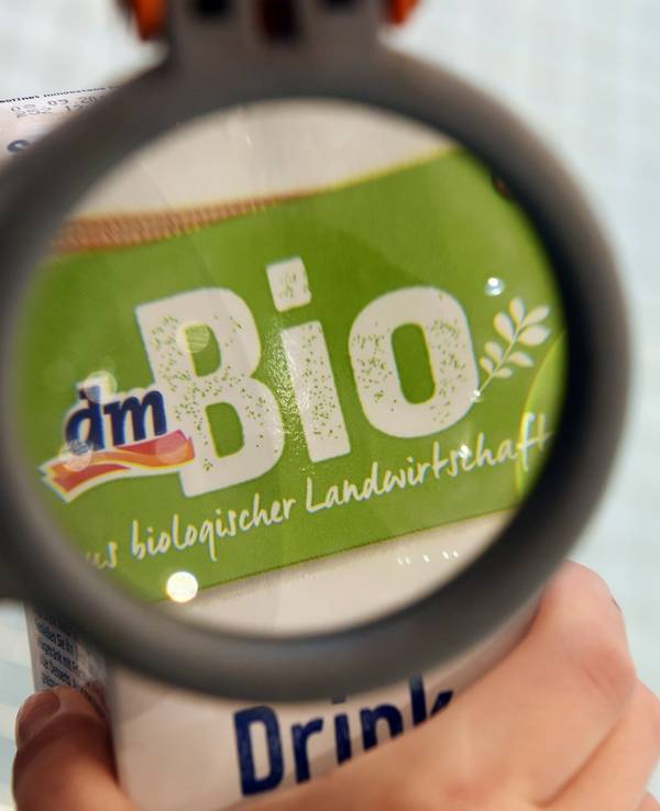 Eine Person betrachtet in einer Filiale der Drogeriemarktkette dm durch eine Lupe an einem Einkaufswagen ein dm-Bioprodukt.