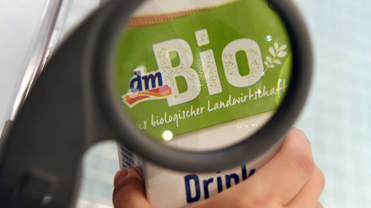 Eine Person betrachtet in einer Filiale der Drogeriemarktkette dm durch eine Lupe an einem Einkaufswagen ein dm-Bioprodukt.