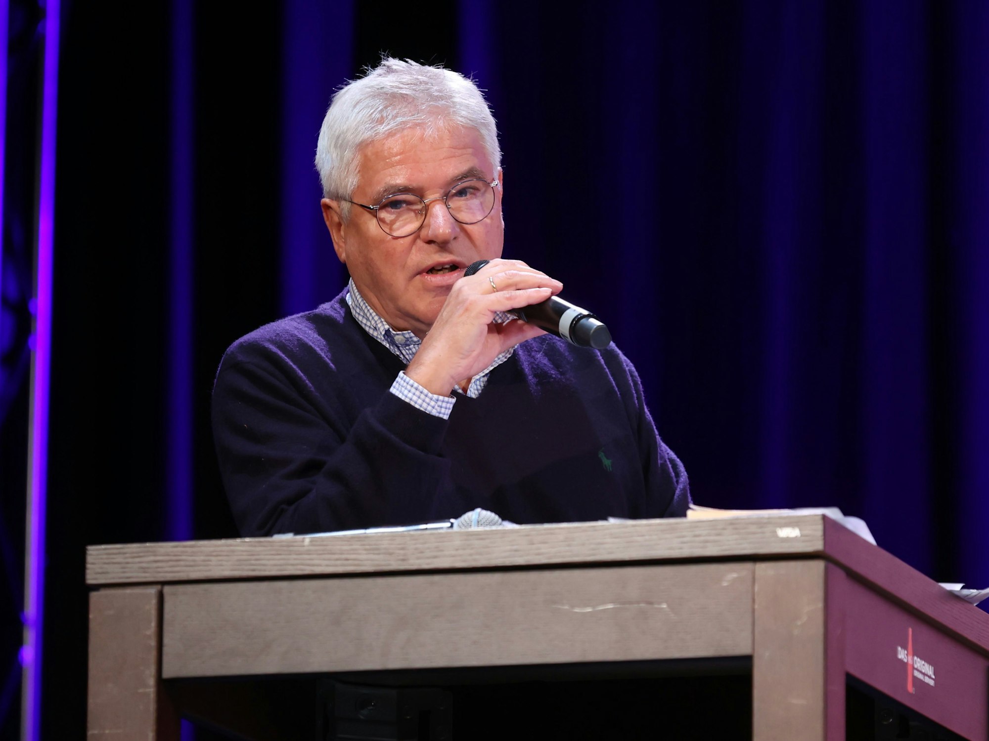 Axel Molinski, Geschäftsführer der Volksbühne am Rudolfplatz, sitzt mit Mikrofon an einem Pult und spricht.