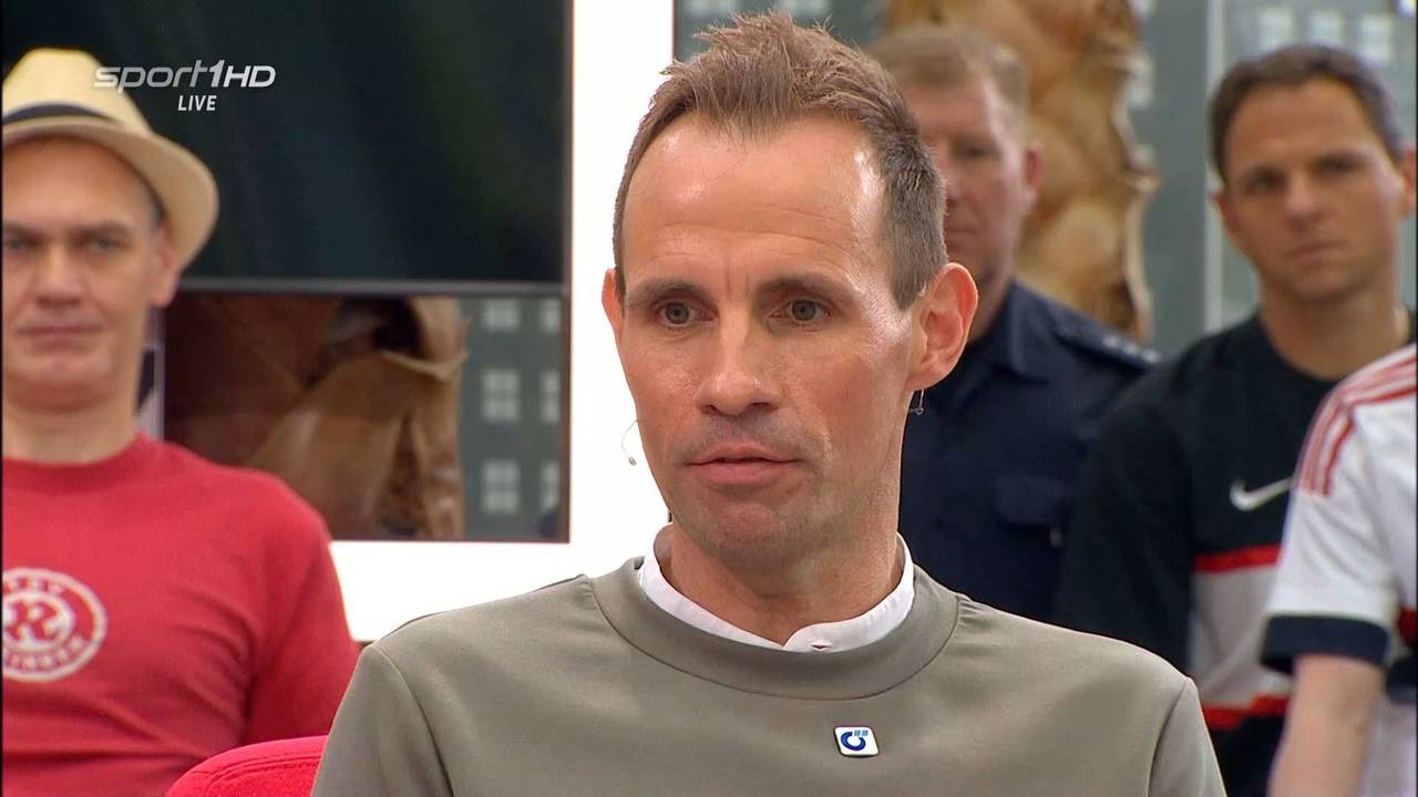 Sascha Stegemann sitzt als Gast beim Doppelpass. Im Hintergrund ist ein uniformierter Polizist zu sehen.