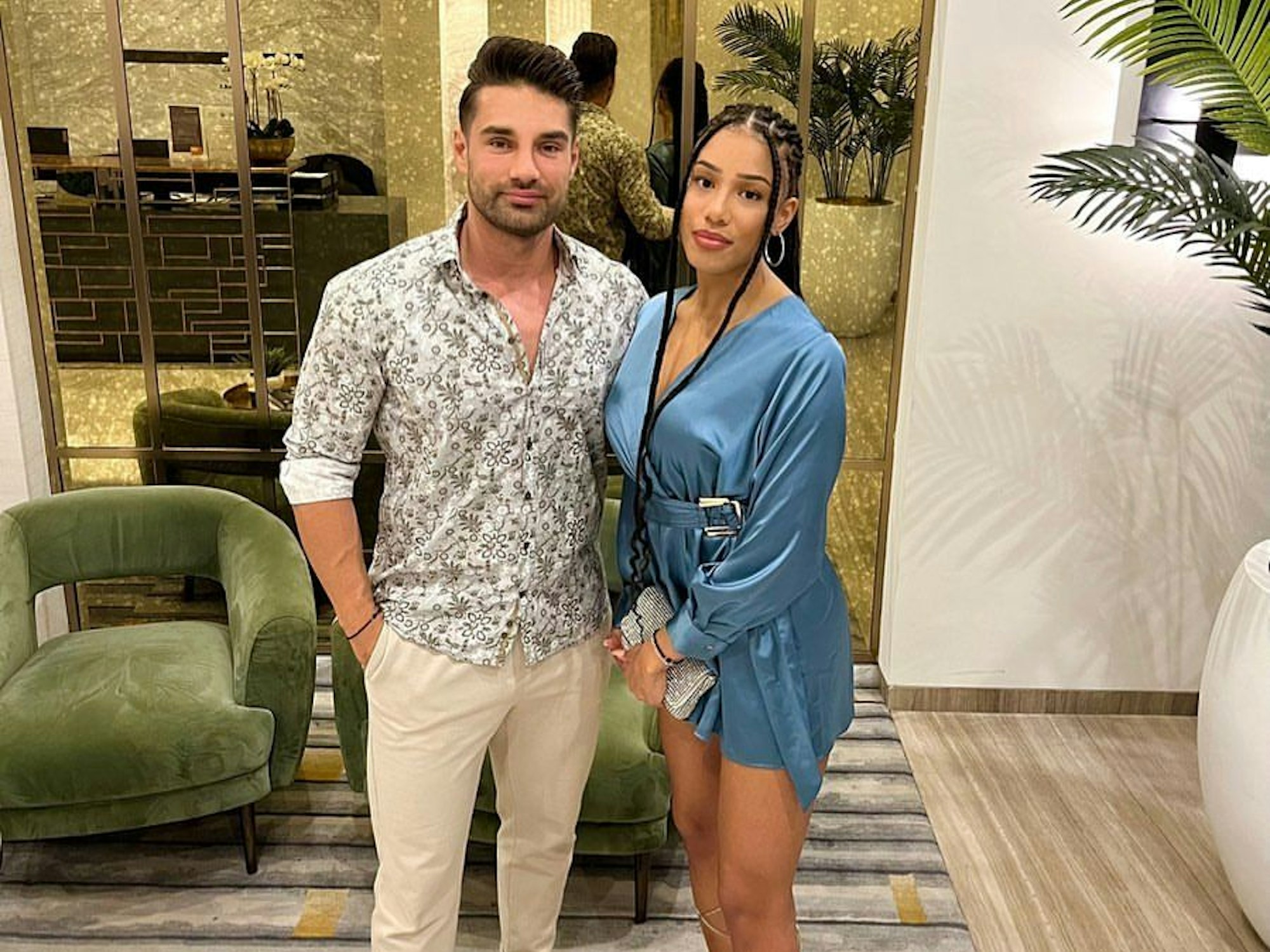 Aleksandar Petrović, hier in beige Hose und gemustertem Hemd, und Vanessa Nwattu, hier im blauen Minikleid, blicken in die Kamera.