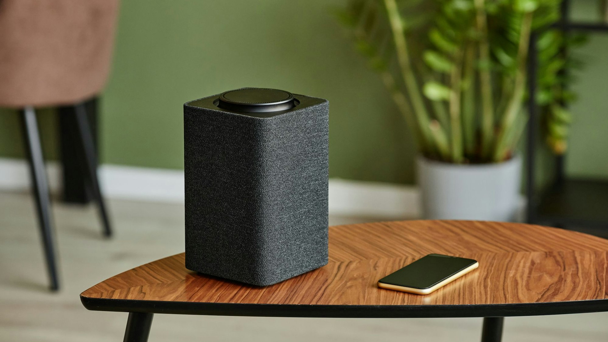 Ein WLAN-Lautsprecher steht neben einem Handy auf einem Tisch.