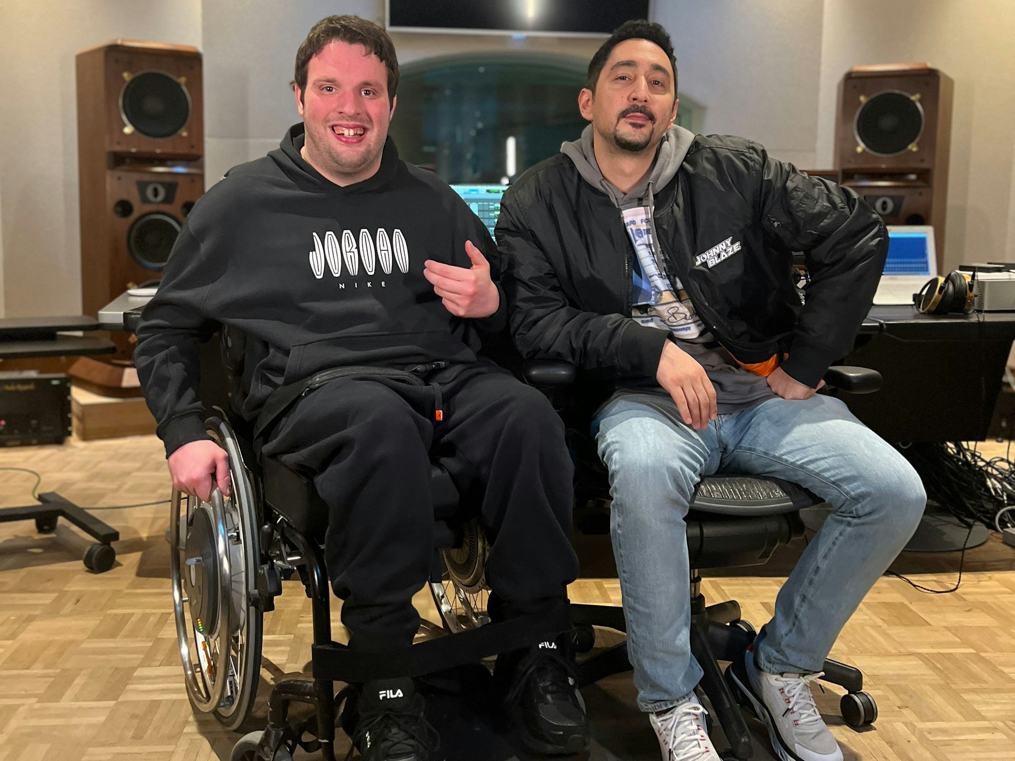 Rapper Rolling G sitzt neben Rapper Eko Fresh. Beide schrieben zusammen einen Song namens „Neue Wege“ und möchten auf die fehlende Barrierefreiheit in Deutschland aufmerksam machen.