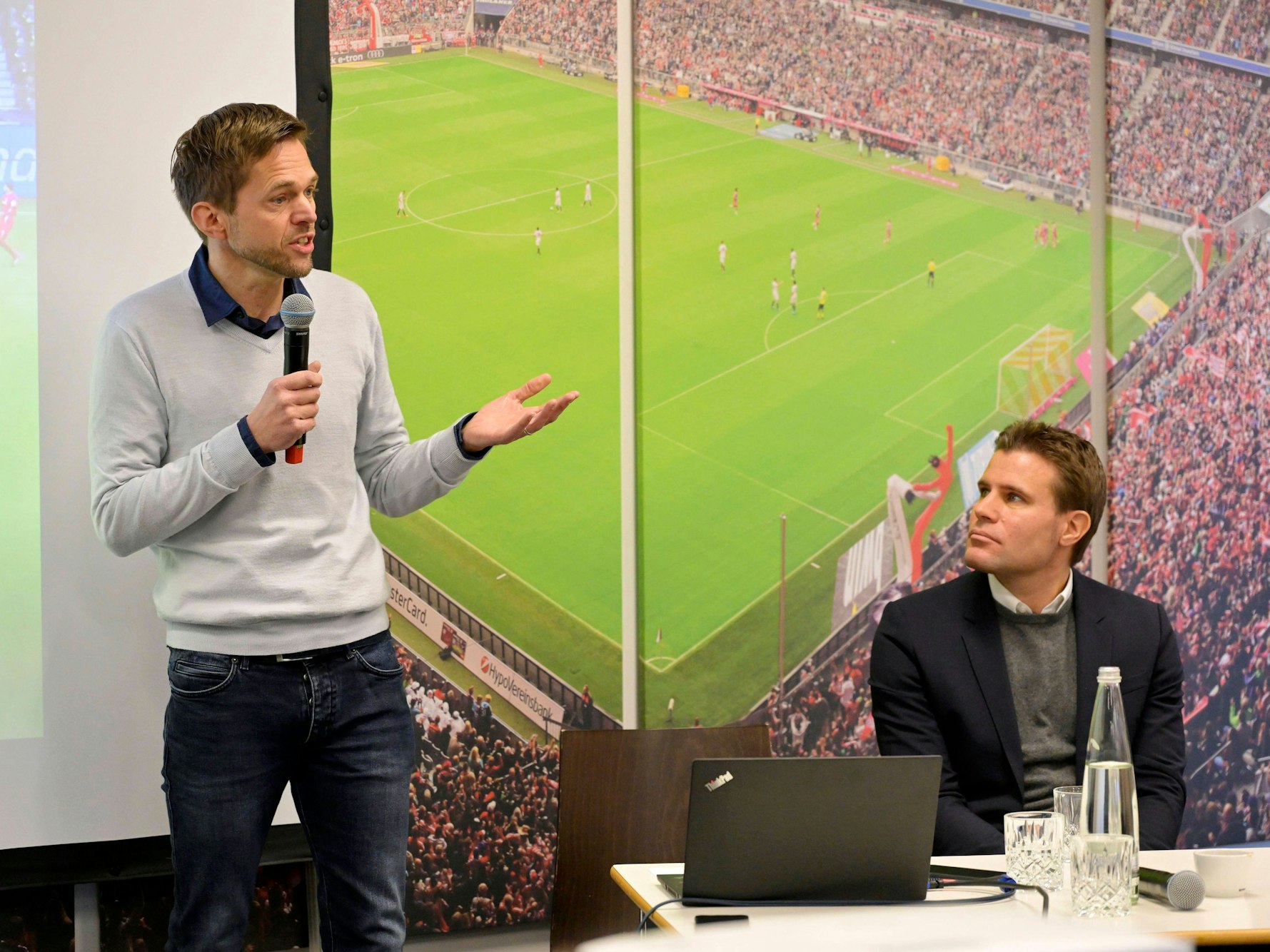 Jochen Drees (links) spricht ins Mikrofon, Felix Brych schaut ihm zu.