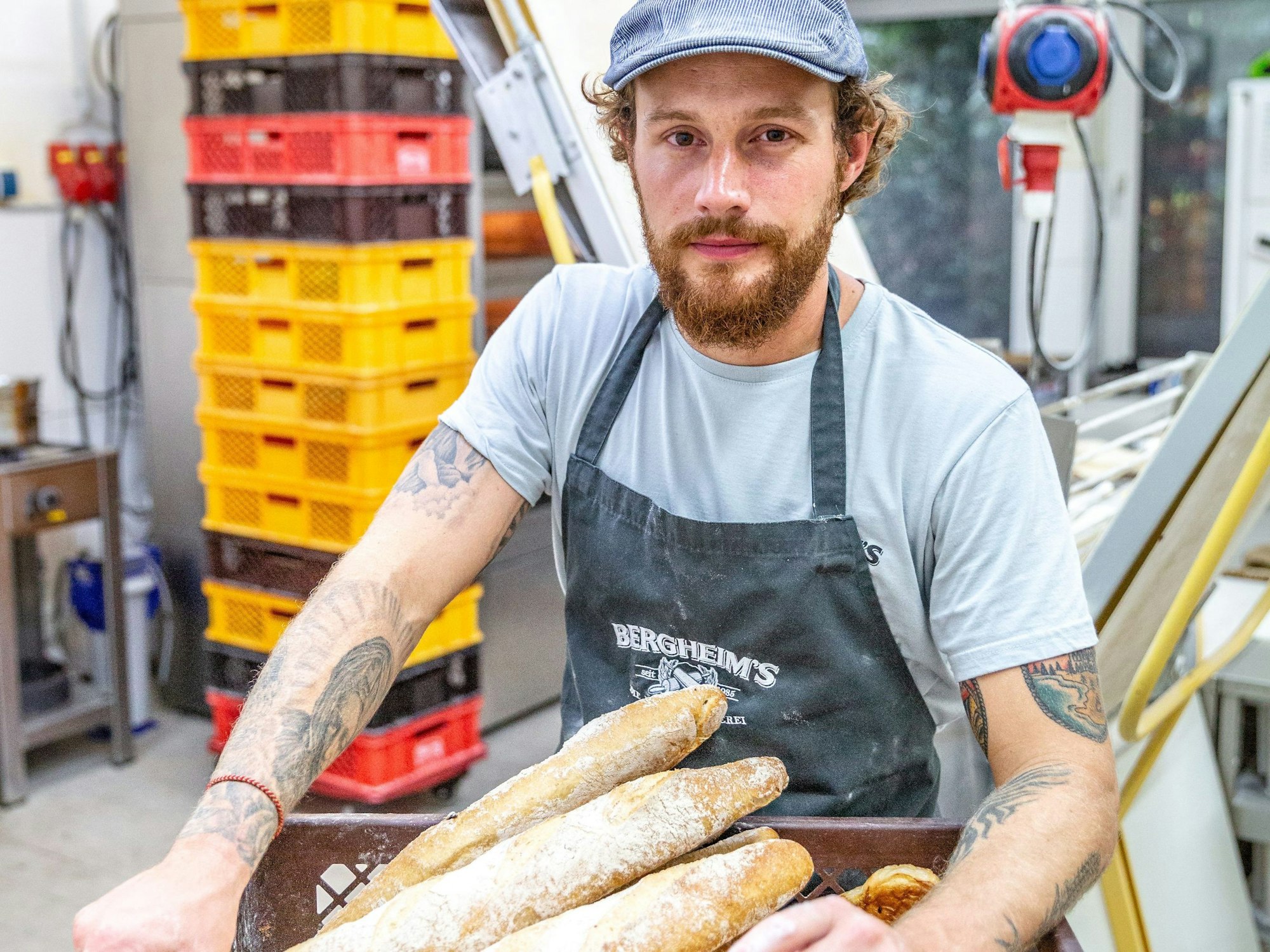 Bäckermeister Tim Bergheim steht mit einem Korb voller Ciabatta-Brote in der Backstube der Bäckerei „Bergheim's – Die Meisterbäckerei“.