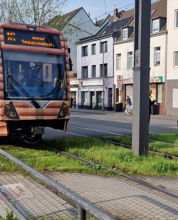 Einsatzkräfte stehen neben einem Auto, dessen Fahrerseite stark beschädigt ist. Auf den Gleisen neben an steht eine Straßenbahn.