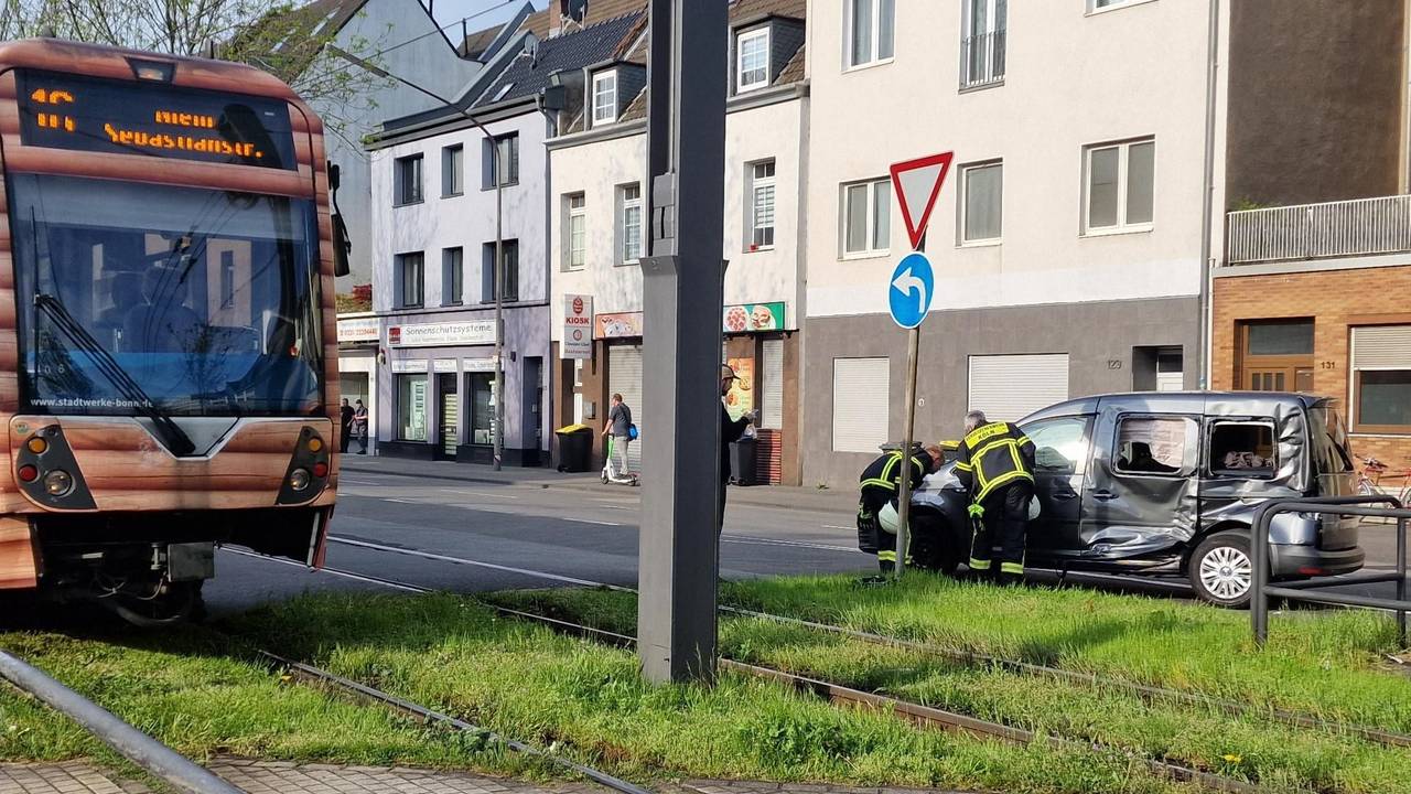 Einsatzkräfte stehen neben einem Auto, dessen Fahrerseite stark beschädigt ist. Auf den Gleisen neben an steht eine Straßenbahn.