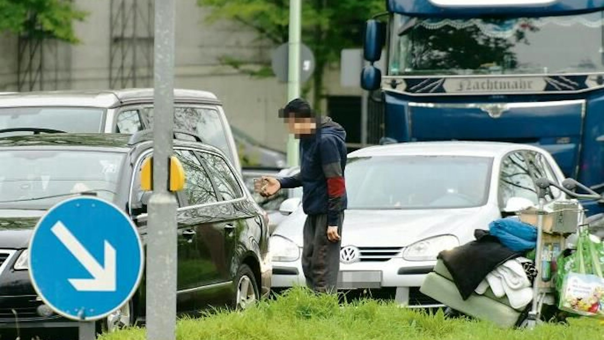 Ein Obdachloser bettelt zwischen Autos am Rheinufer um etwas Geld.