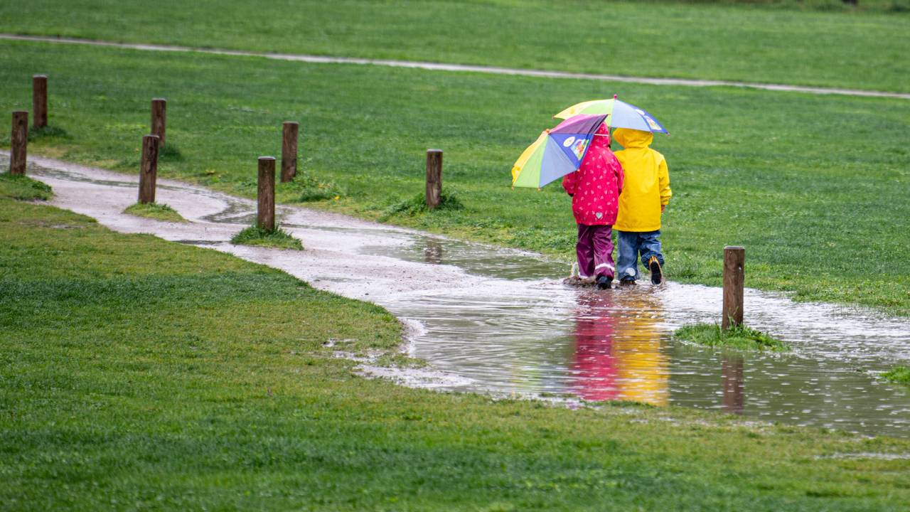 Zwei Kinder laufen in unserem Symbolbild einem Park durch eine große Pfütze. Im Westen Deutschlands lässt Starkregen die Flüsse steigen.