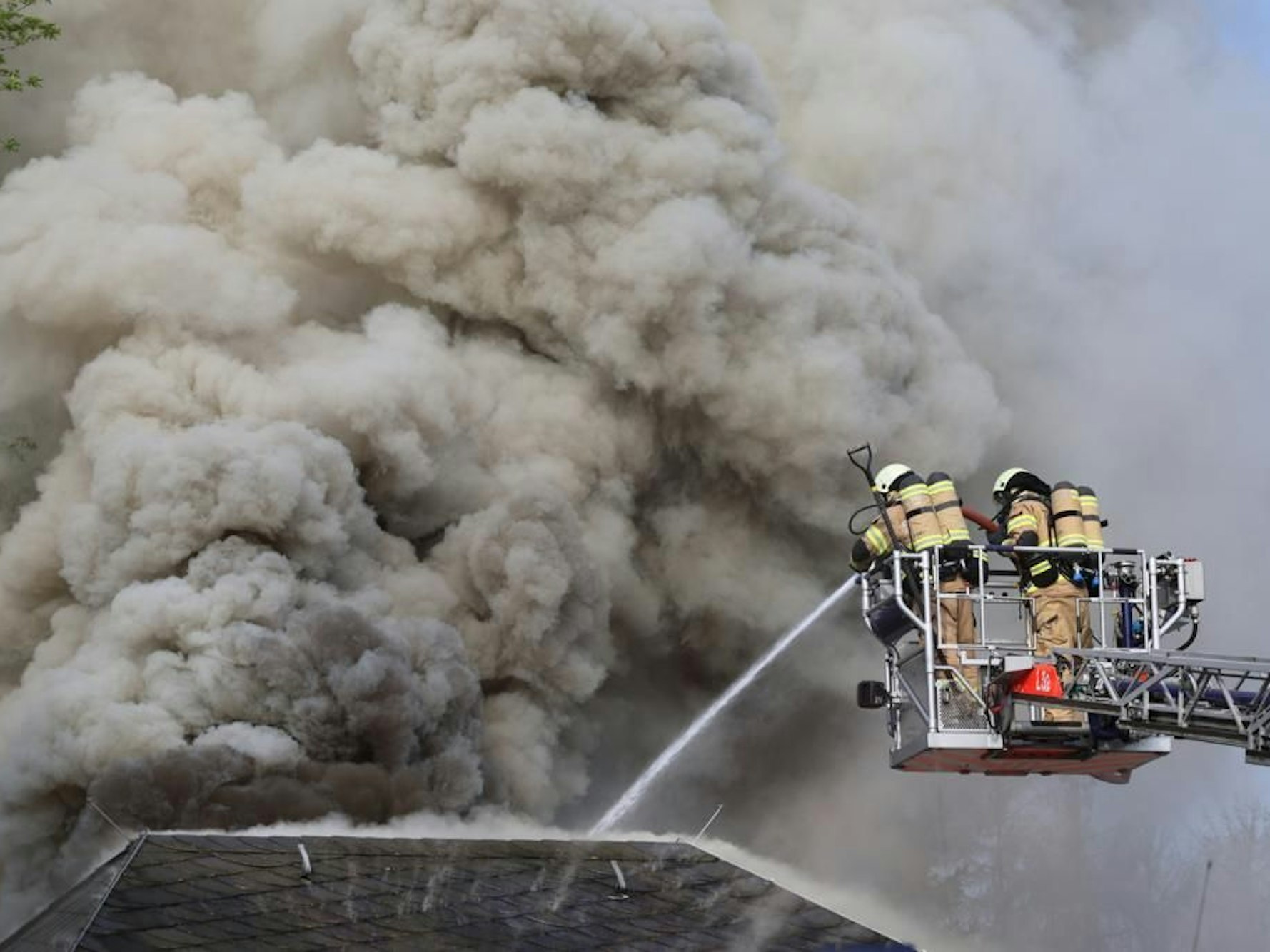 Das Feuer im Stadtteil Bärbroich von Bergisch Gladbach; Feuerwehr im Einsatz bei einem Brand in Bergisch Gladbach. Hohe Rauchwolken steigen aus dem Haus.