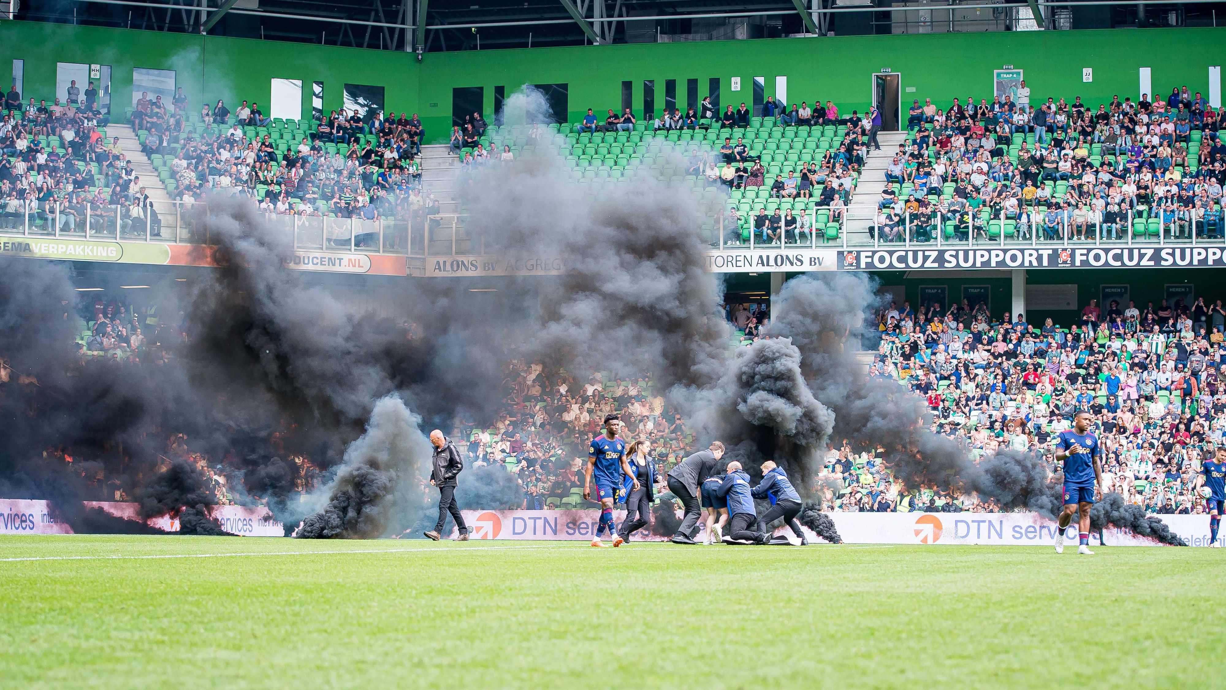 Fans des FC Groningen werfen während des Spiels Rauchbomben auf das Spielfeld und einige Fans, die auf das Spielfeld gelaufen sind, werden von Ordnern festgehalten.