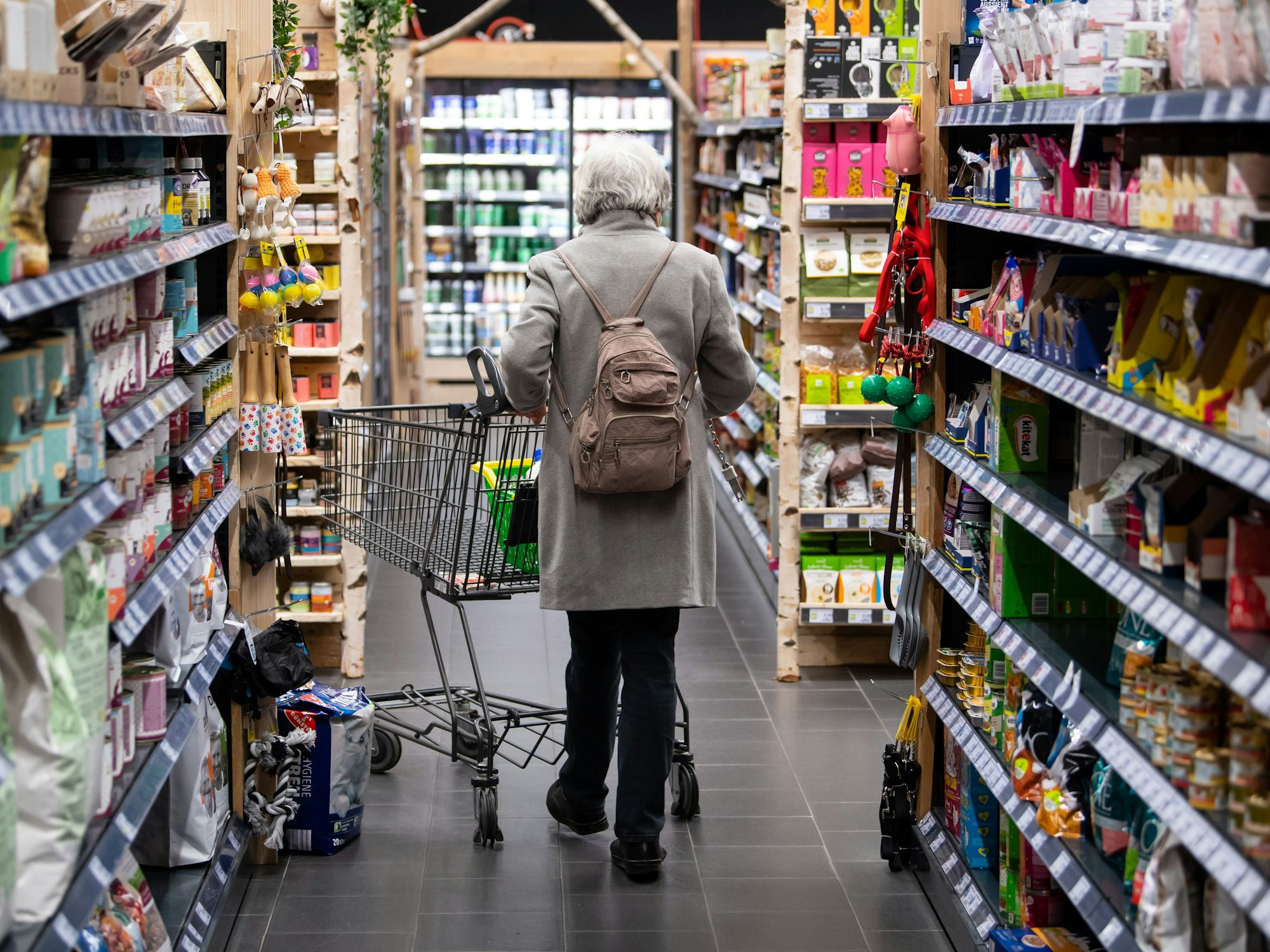 Eine Frau geht mit ihrem Einkaufswagen durch einen Supermarkt.
