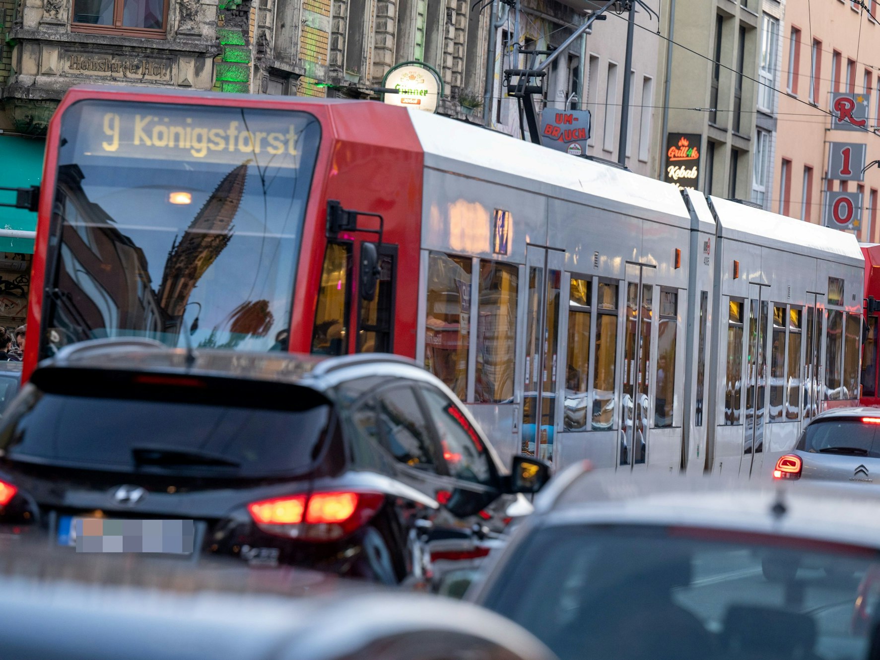 Eine Straßenbahn der Linie 9 nach Königsforst fährt über eine Straße, auf der sich der Autoverkehr staut.