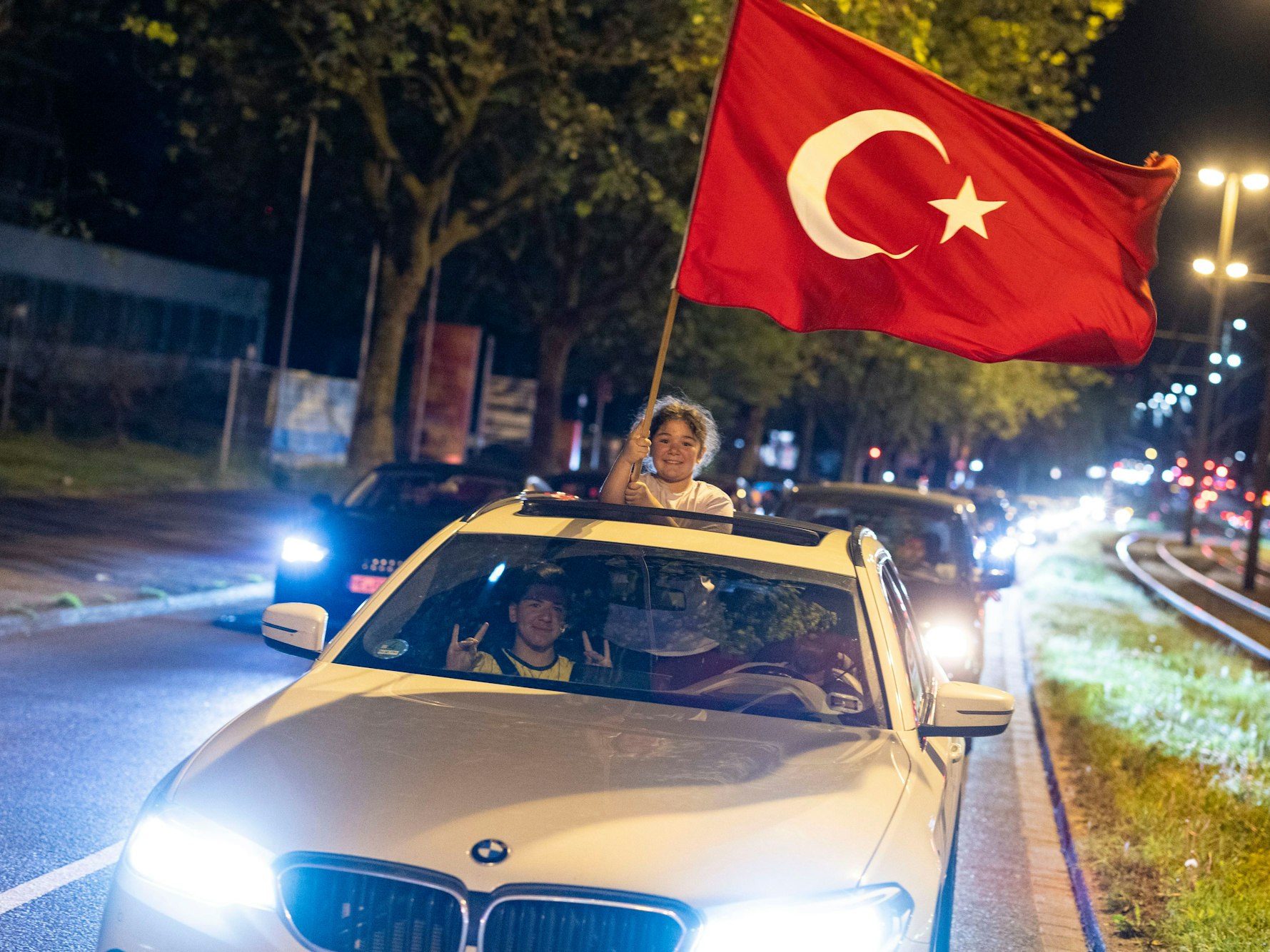 Ein Mädchen hält aus einem fahrenden Auto eine Türkei-Flagge und freut sich