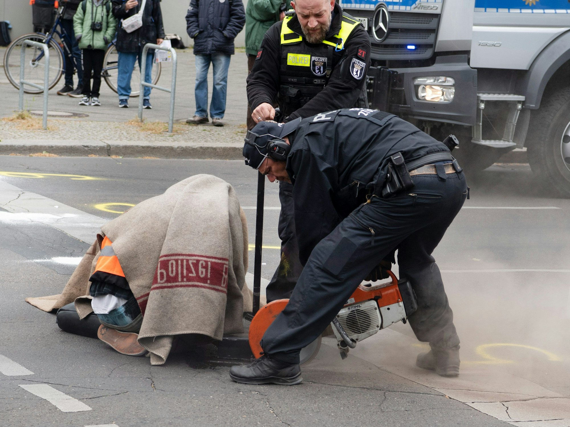 Polizeikräfte versuchen bei einer Straßenblockade der „Letzten Generation“, Carla Hinrichs, Sprecherin der Umweltschutzgruppe, von der Straße zu lösen.