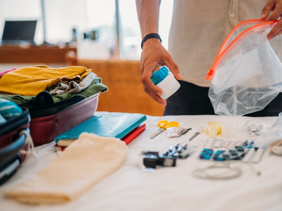 Ein Mann packt Klamotten und Tabletten für den Urlaub.