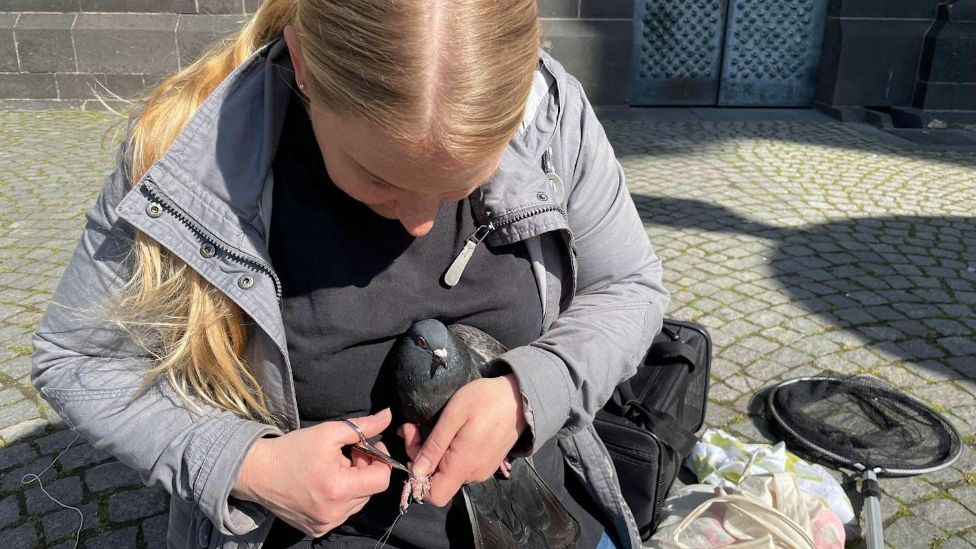 Janina Wisbar hält eine Taube im Arm und schneidet ihr mit einer Schere die Verschnürungen an den Füßen ab.