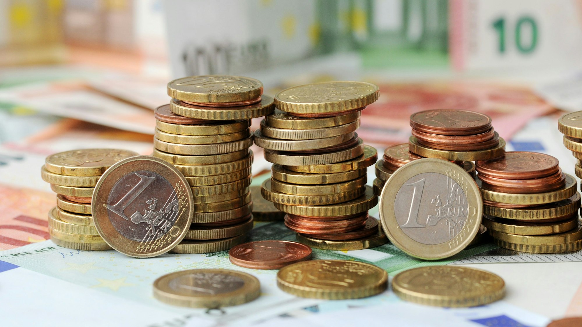Gestapelte Geldmünzen liegen auf Geldscheinen.