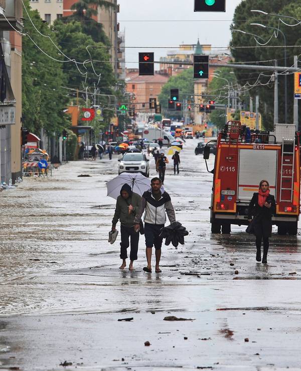 Menschen bahnen sich am 17. Mai ihren Weg durch eine überflutete Straße in Bologna.