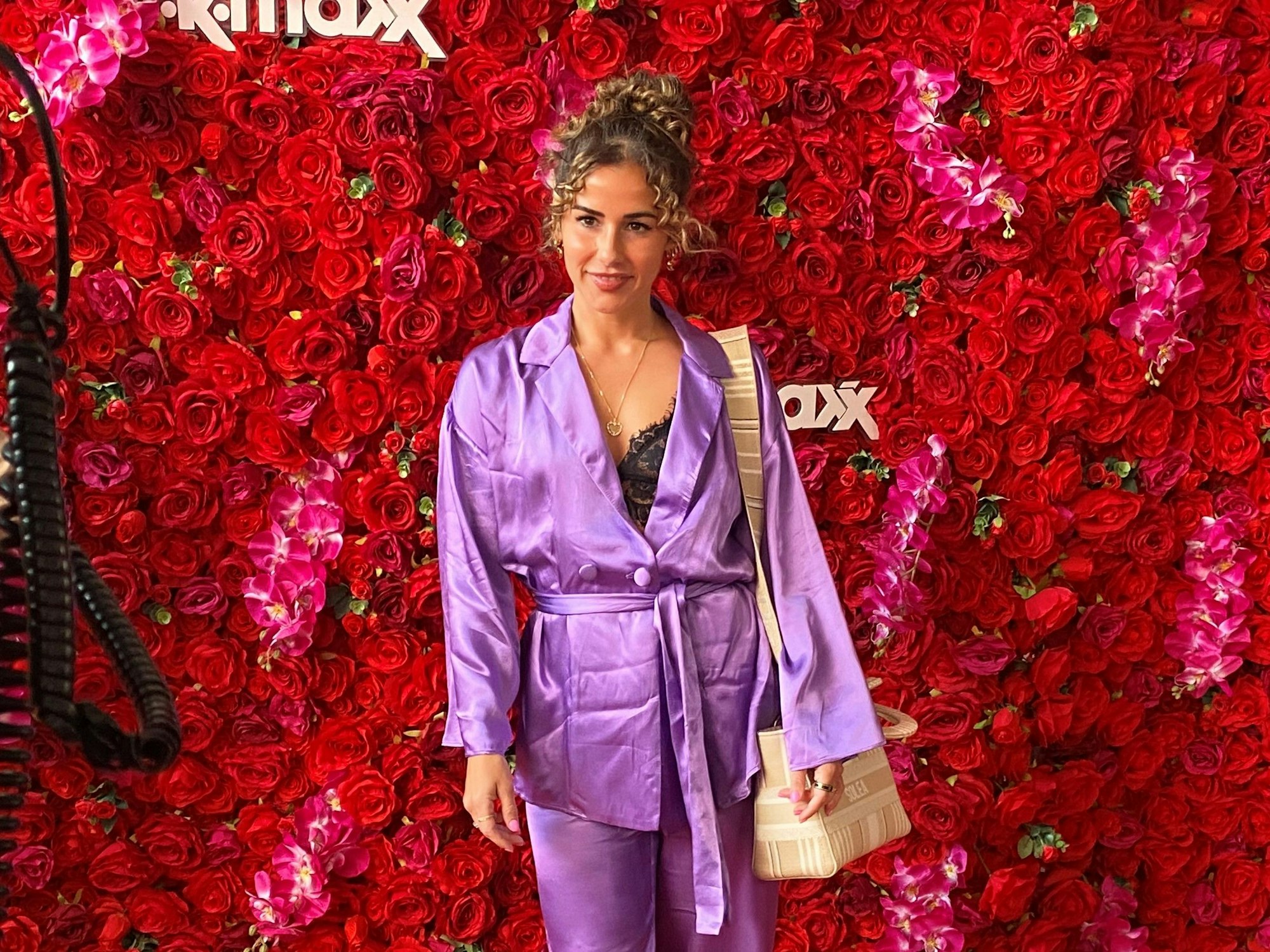 Sarah Engel, posiert vor einer Rosen-Wand für die Kamera.