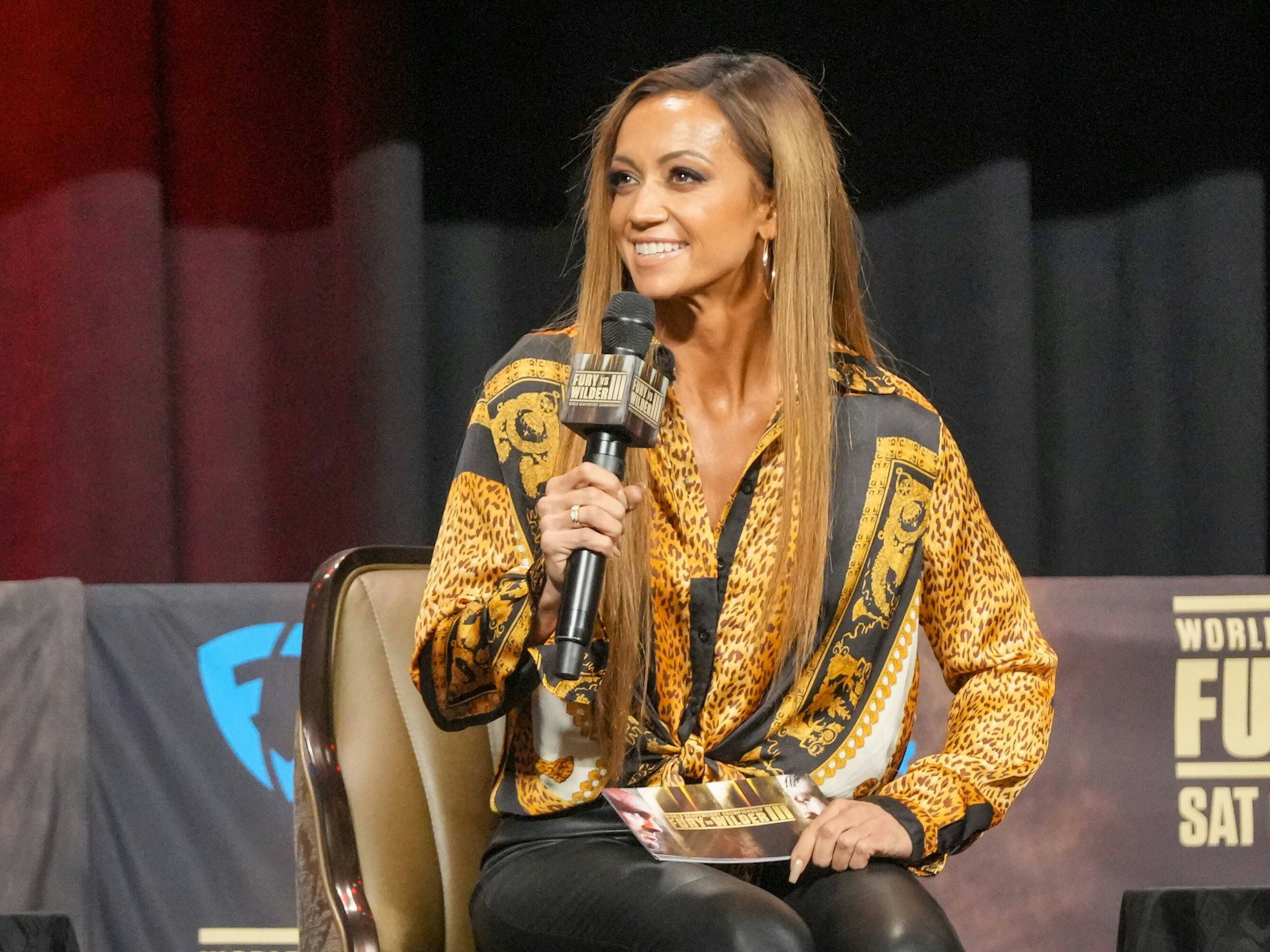 Kate Abdo sitzt auf einem Podium und moderiert.