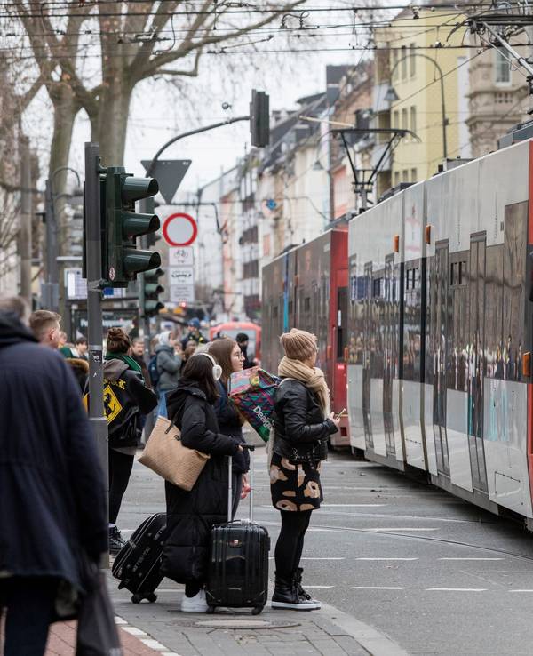 Am Zülpicher Platz fährt eine Bahn der KVB über die Gleise, daneben warten Fußgängerinnen und Fußgänger.