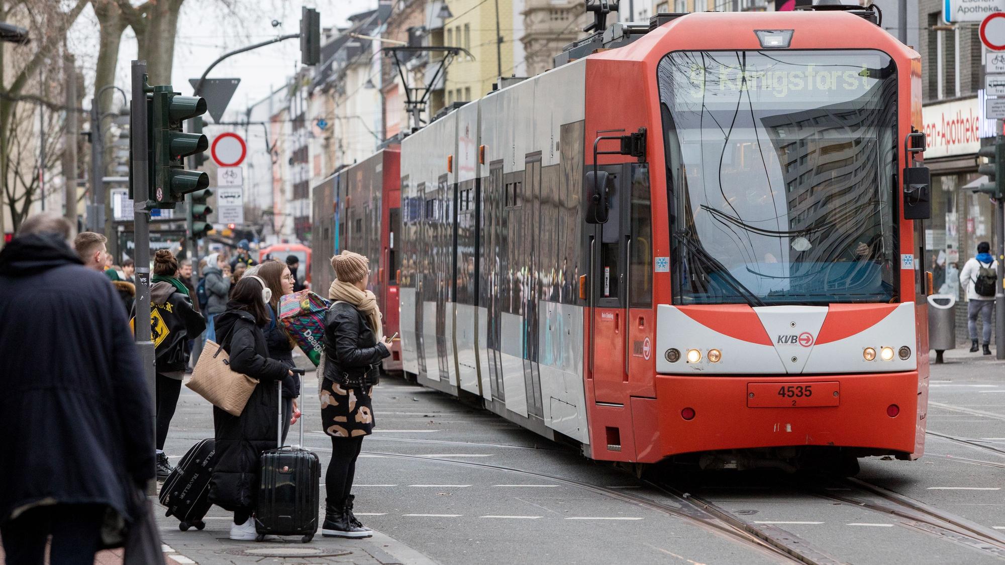 Am Zülpicher Platz fährt eine Bahn der KVB über die Gleise, daneben warten Fußgängerinnen und Fußgänger.