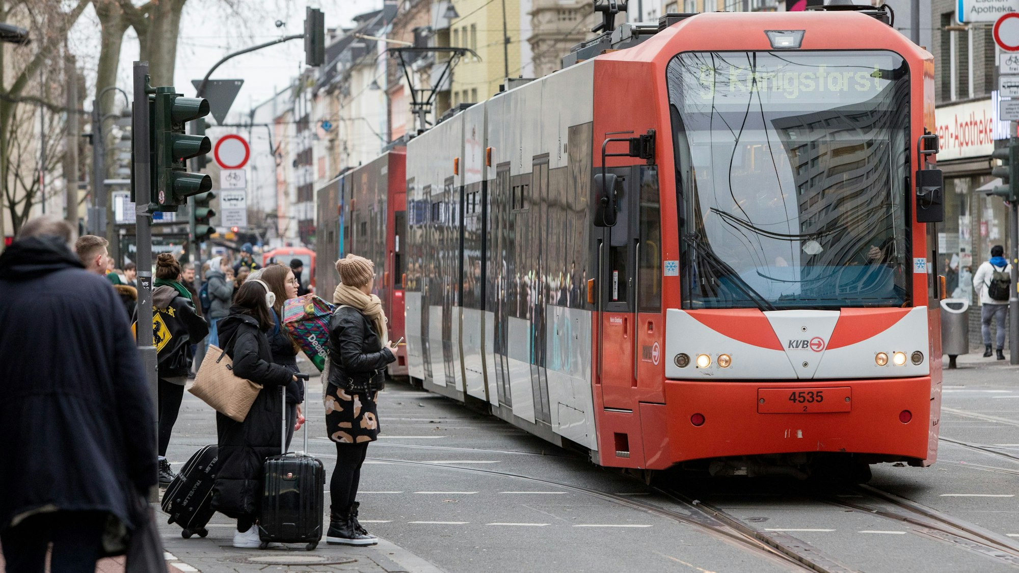 Am Zülpicher Platz fährt eine Bahn der KVB über die Gleise, daneben warten Fußgängerinnen und Fußgänger.