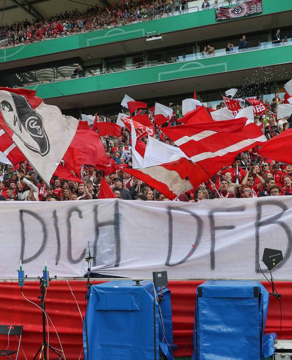 Die Fans des SC Freiburg schwenken Fahnen und präsentieren ein kritisches DFB-Banner.