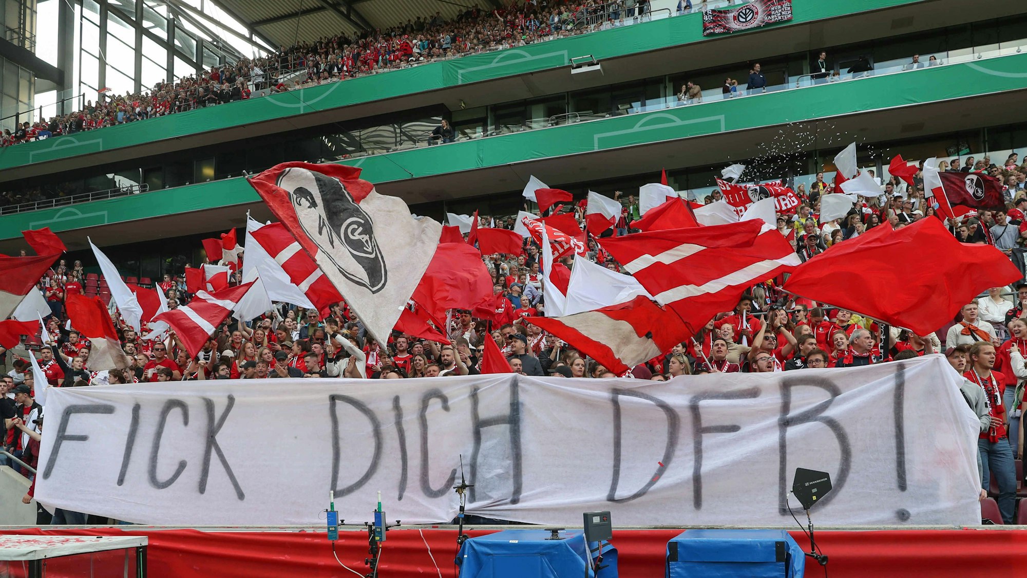 Die Fans des SC Freiburg schwenken Fahnen und präsentieren ein kritisches DFB-Banner.